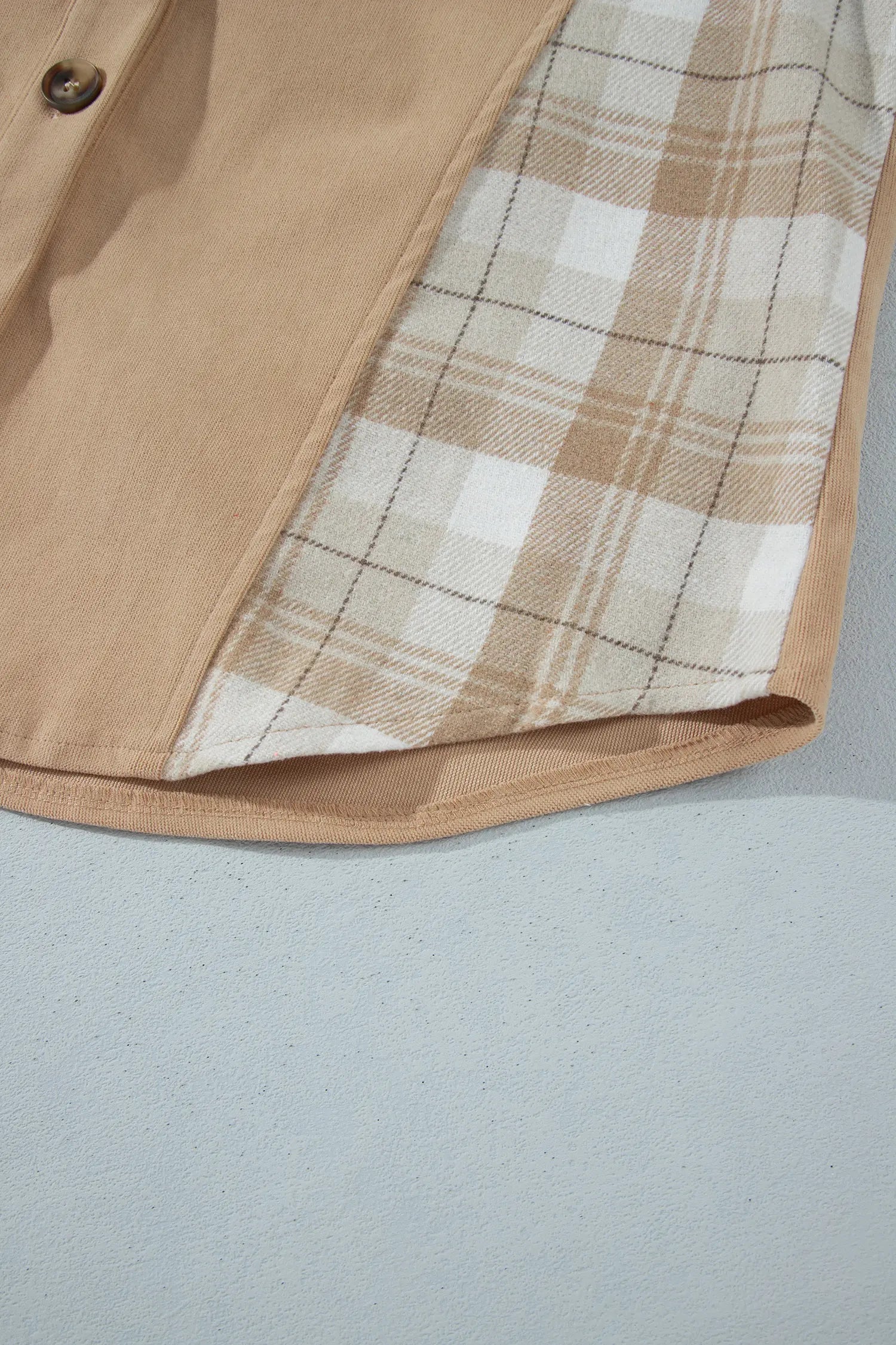 Close-up of a beige buttoned garment corner showing a tan and white plaid lining, set against a light gray background.