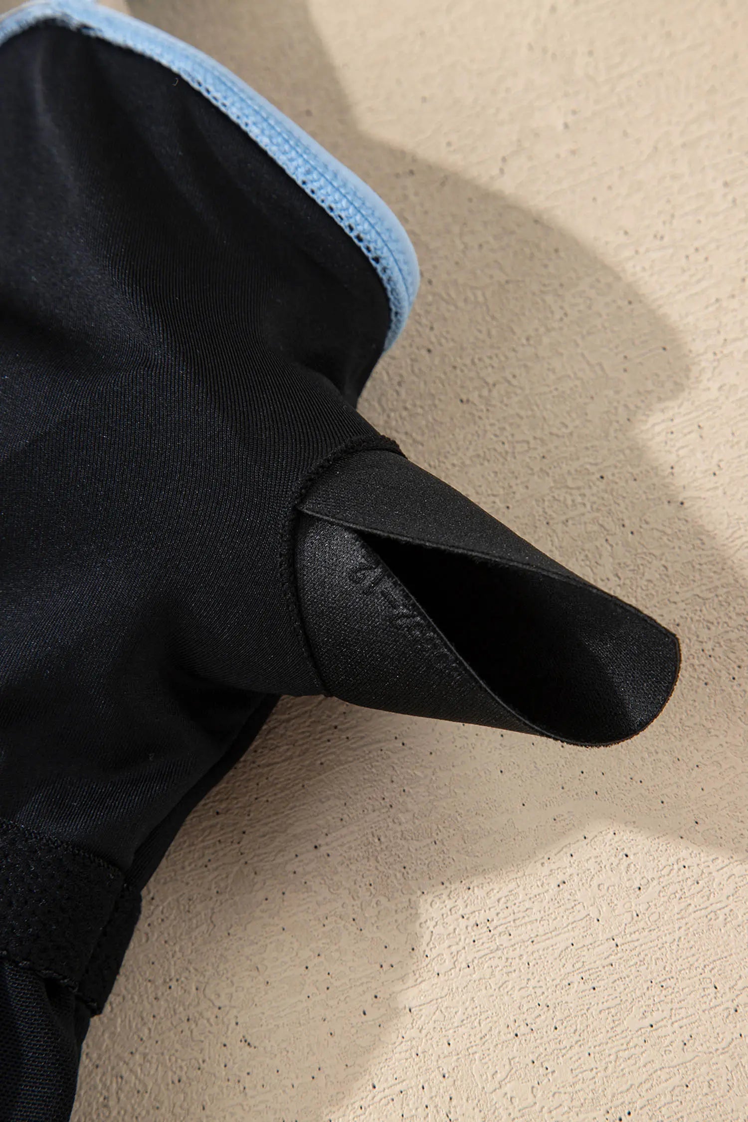 Close-up of a black glove with blue lining on a beige surface