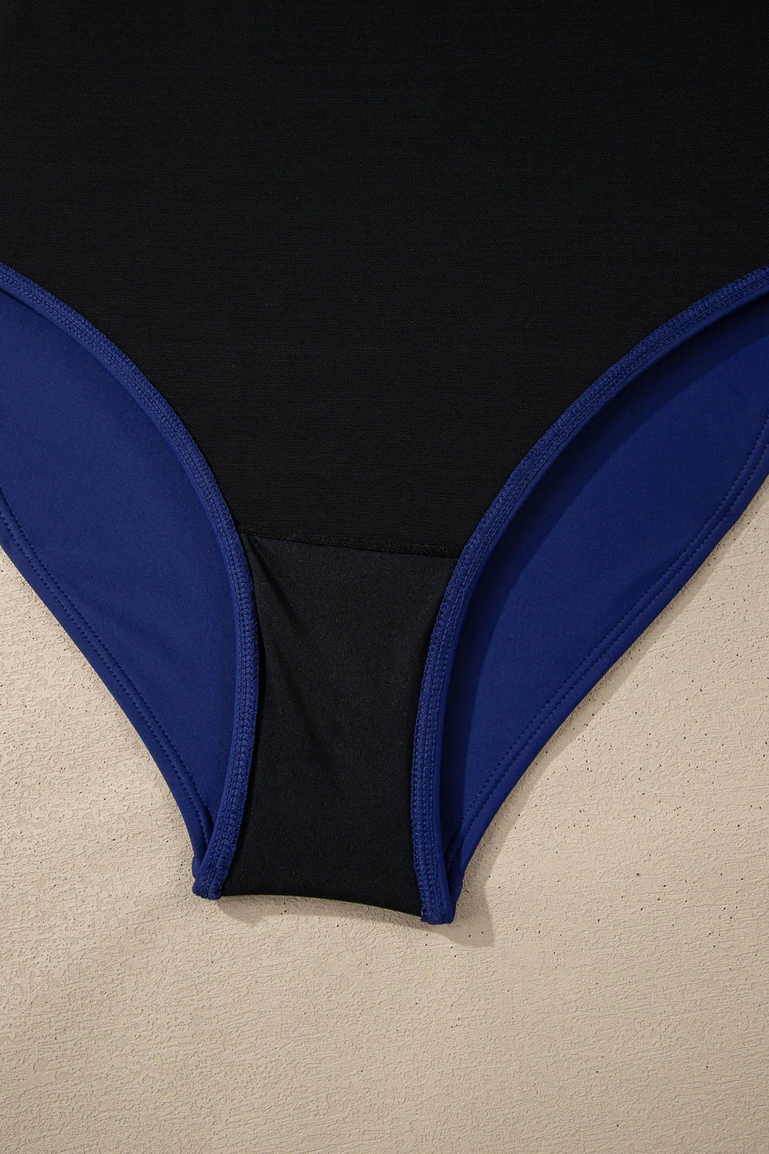 Close-up of a black swimsuit with blue trim on a beige surface