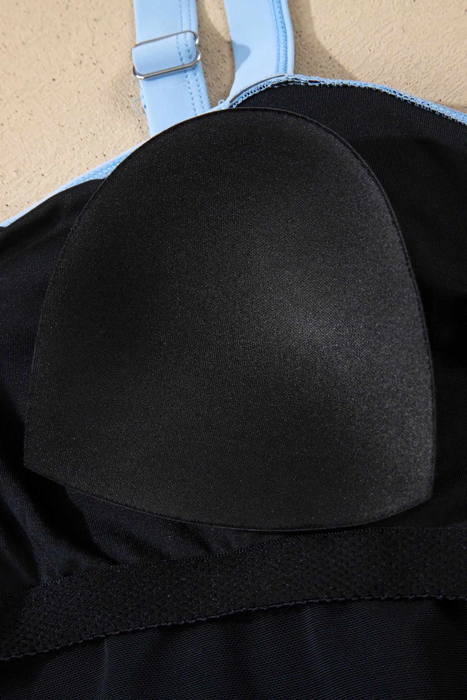 Black bikini top with blue straps on a beige background