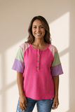 Woman wearing a pink and multicolored top against a beige wall