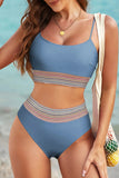 Woman wearing a blue swimsuit with a colorful striped pattern on a beach.