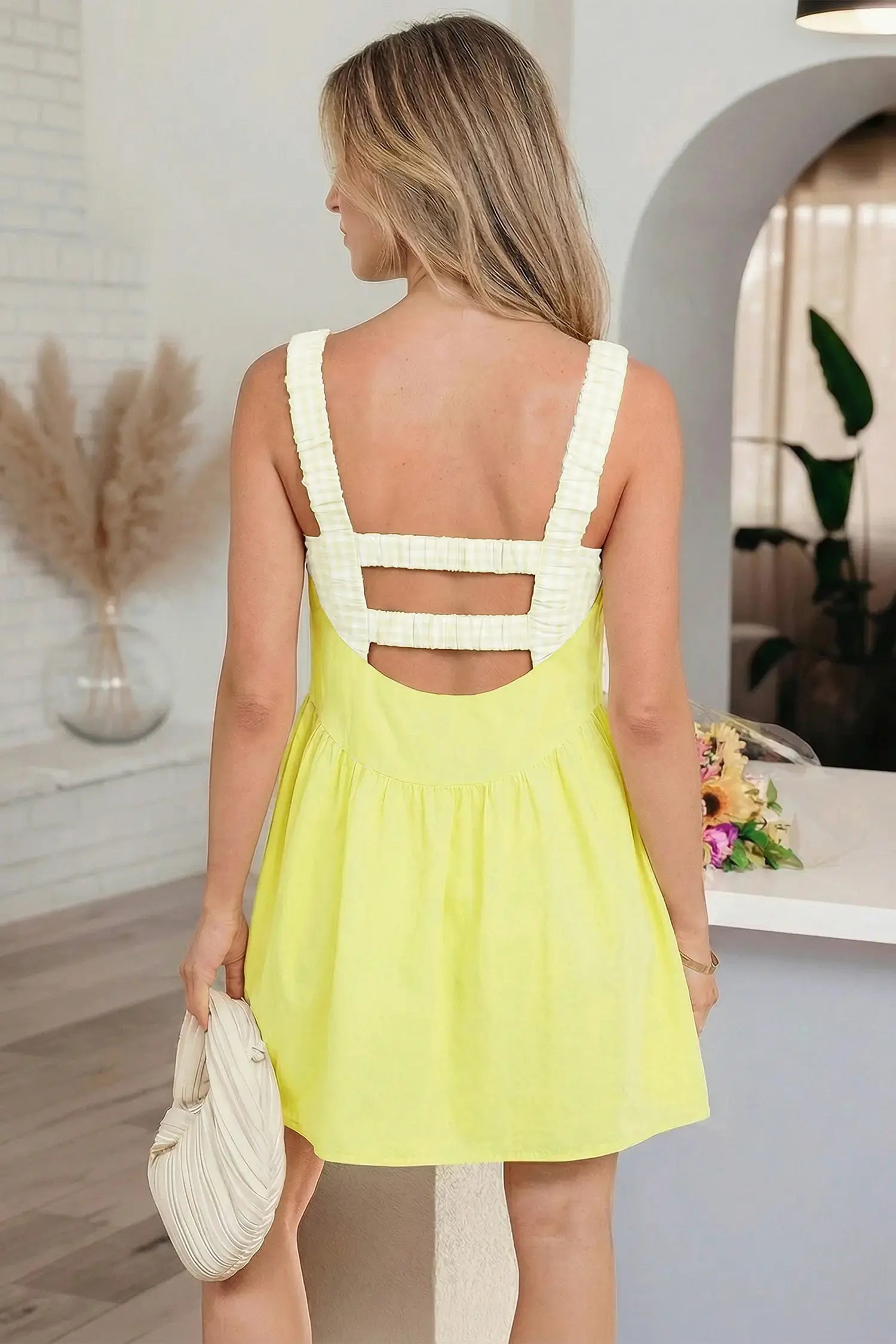 Woman wearing a yellow dress with cut-out back design in an indoor setting.
