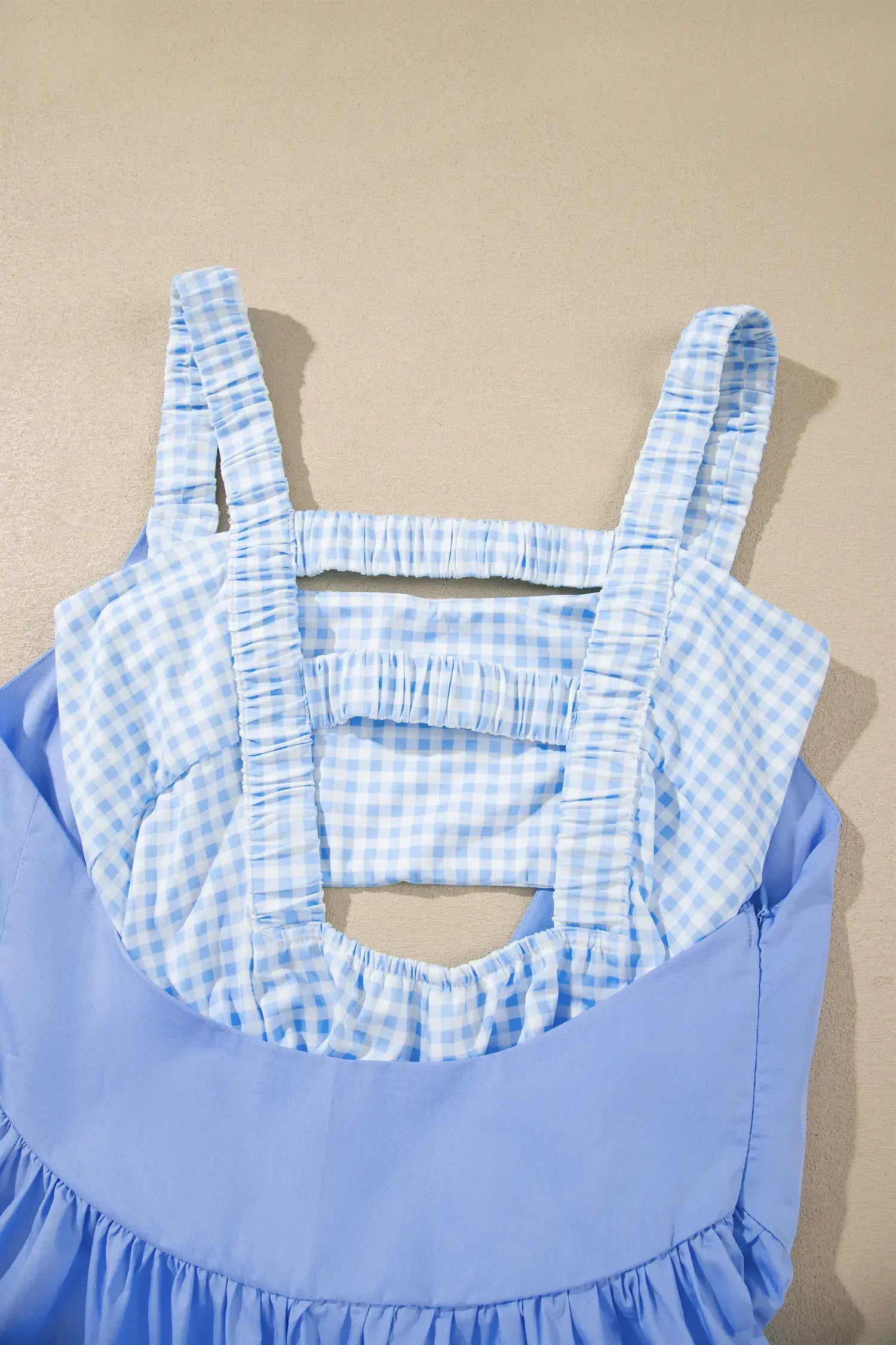 A light blue and white gingham patterned halter top with a solid light blue ruffled bodice and a ruffled hem, shown against a neutral beige background.