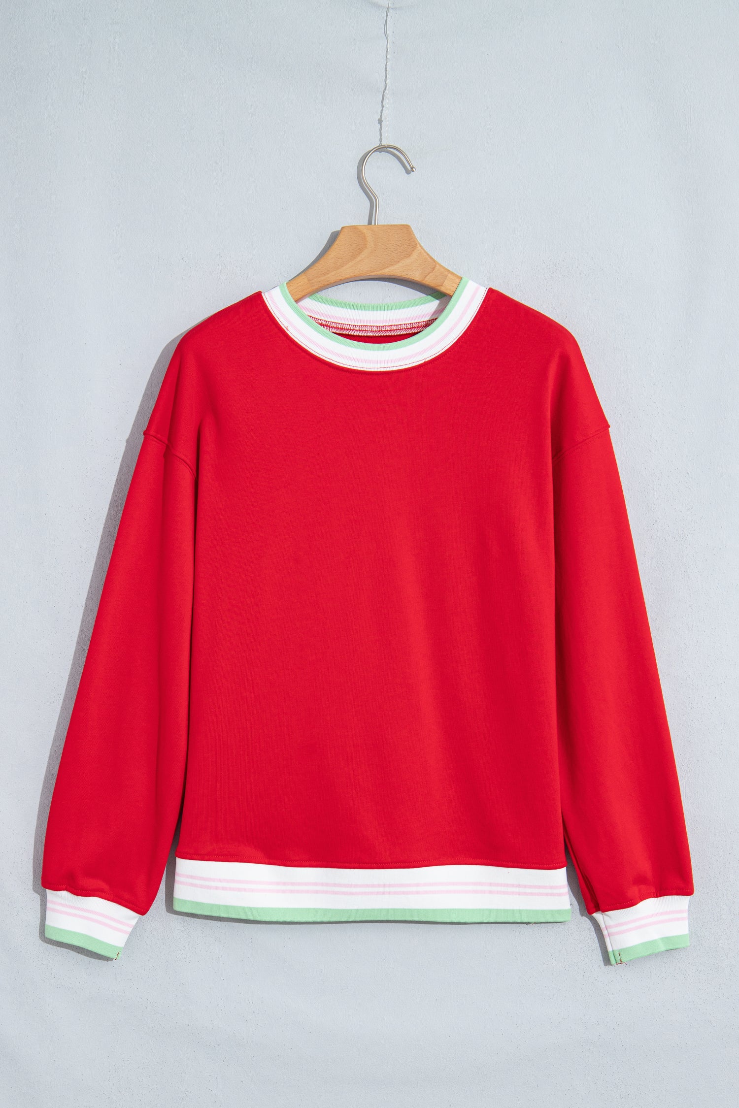 A bright red long-sleeve crewneck sweatshirt hanging on a wooden hanger against a light gray background. 