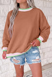Woman in brown sweatshirt with mint-pink striped trim and distressed denim shorts.