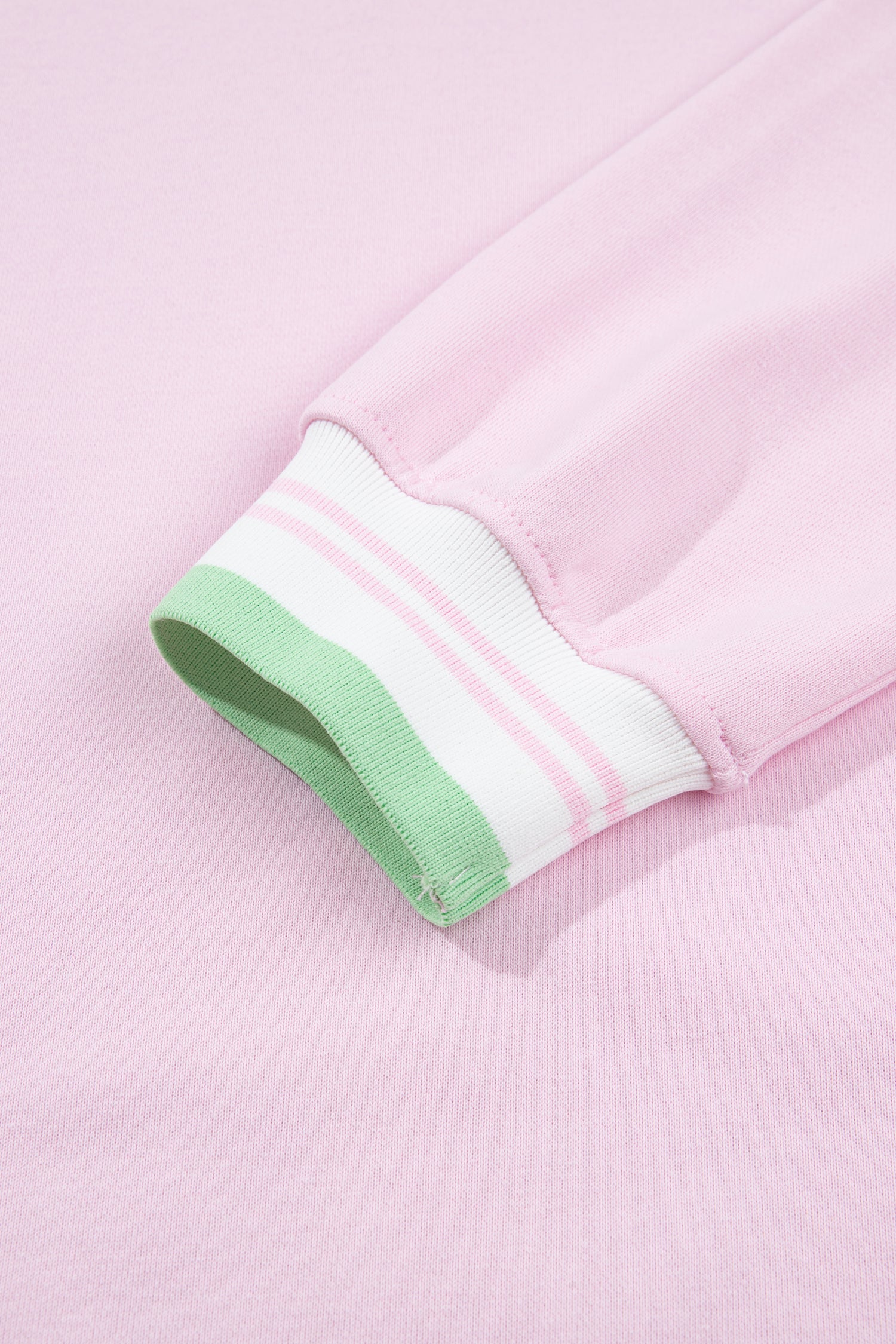 Close-up of a light pink garment cuff with a white ribbed stripe band and a mint green inner lining.