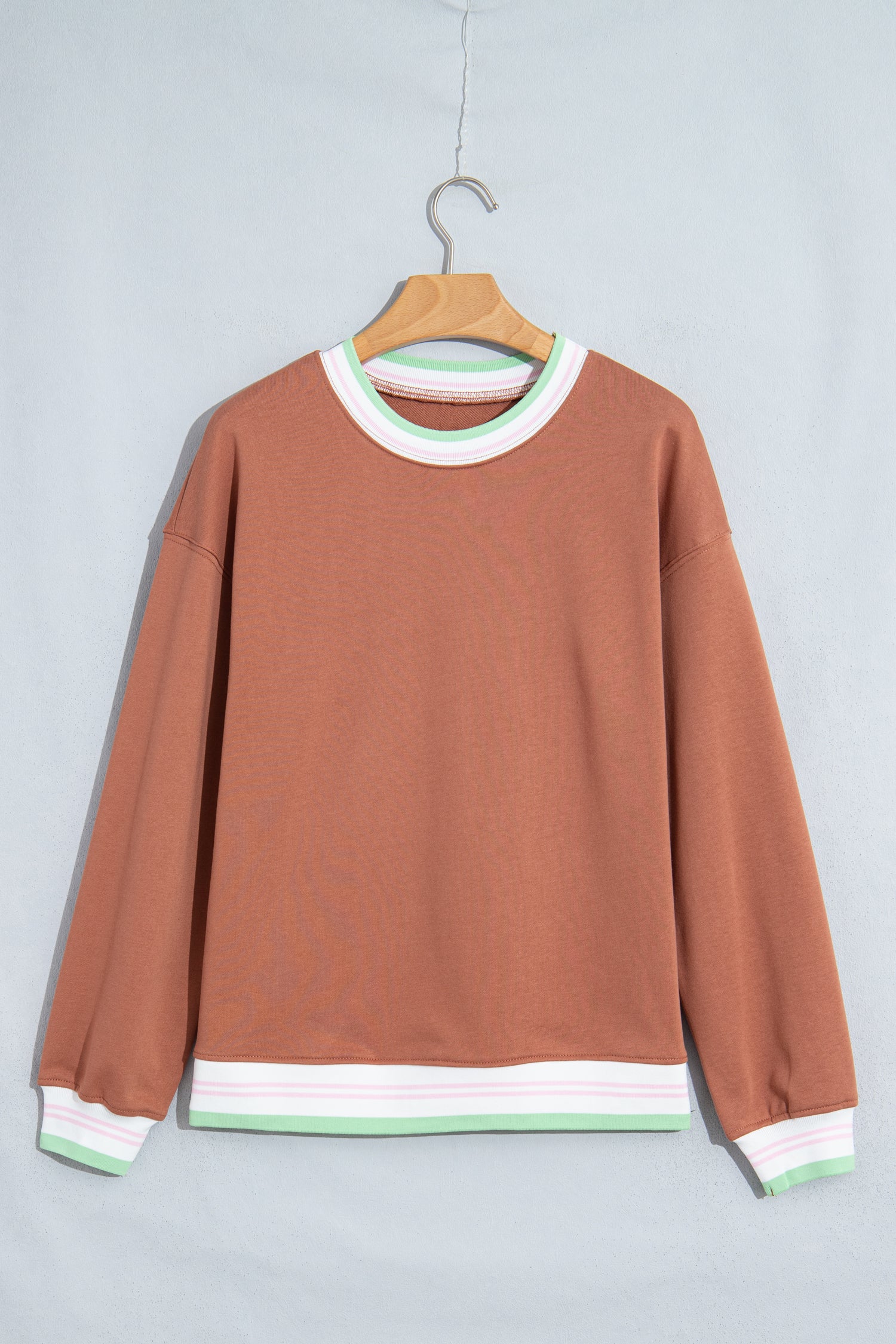 A rust-colored crewneck sweatshirt with white and mint green ribbed trim, 