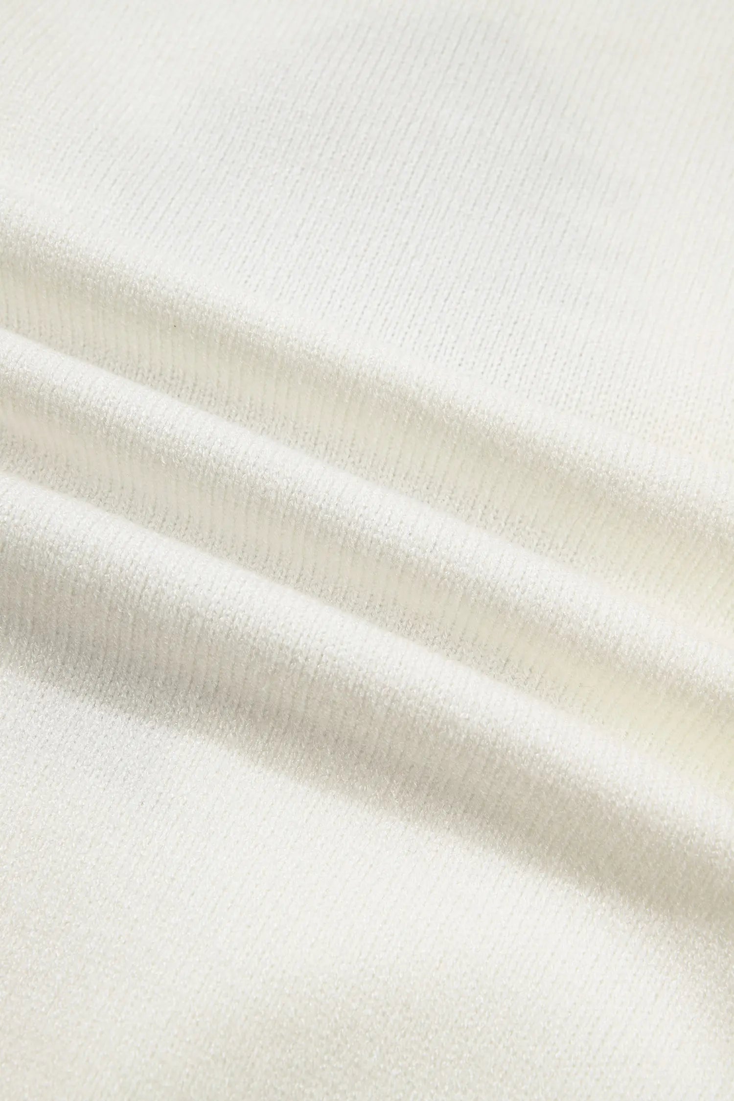 A close-up of a soft, off-white ribbed fabric with gentle folds and a fine knit texture.