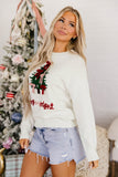 A woman in a “Merry Night” Christmas sweatshirt and denim shorts by a decorated tree.