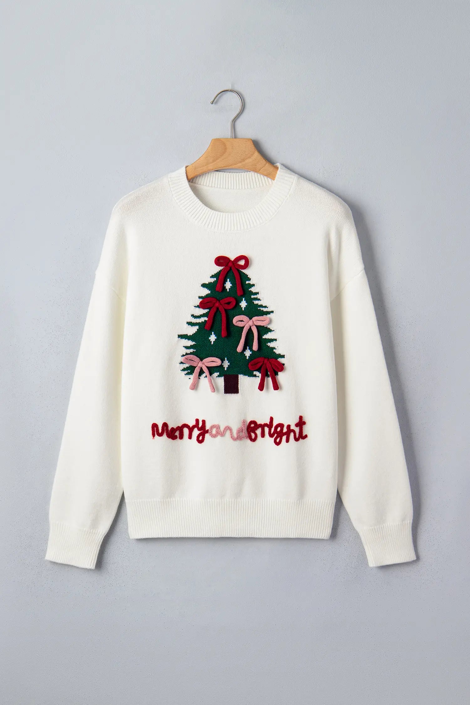 Off-white “Merry and Bright” Christmas sweater with a festive tree graphic on a hanger.