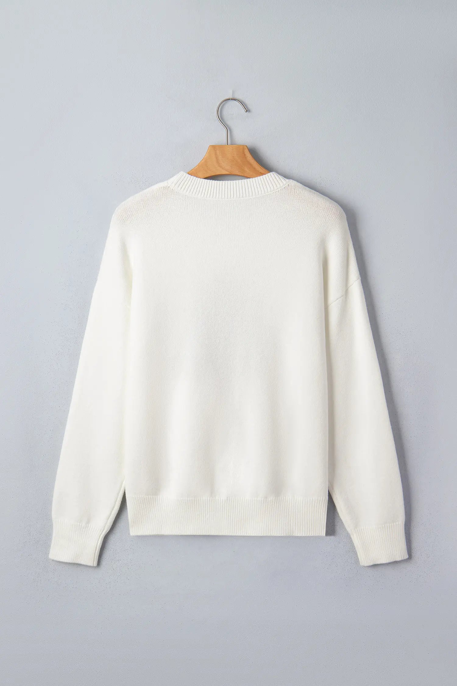 An off-white crewneck knit sweater hanging on a wooden hanger against a solid gray background.