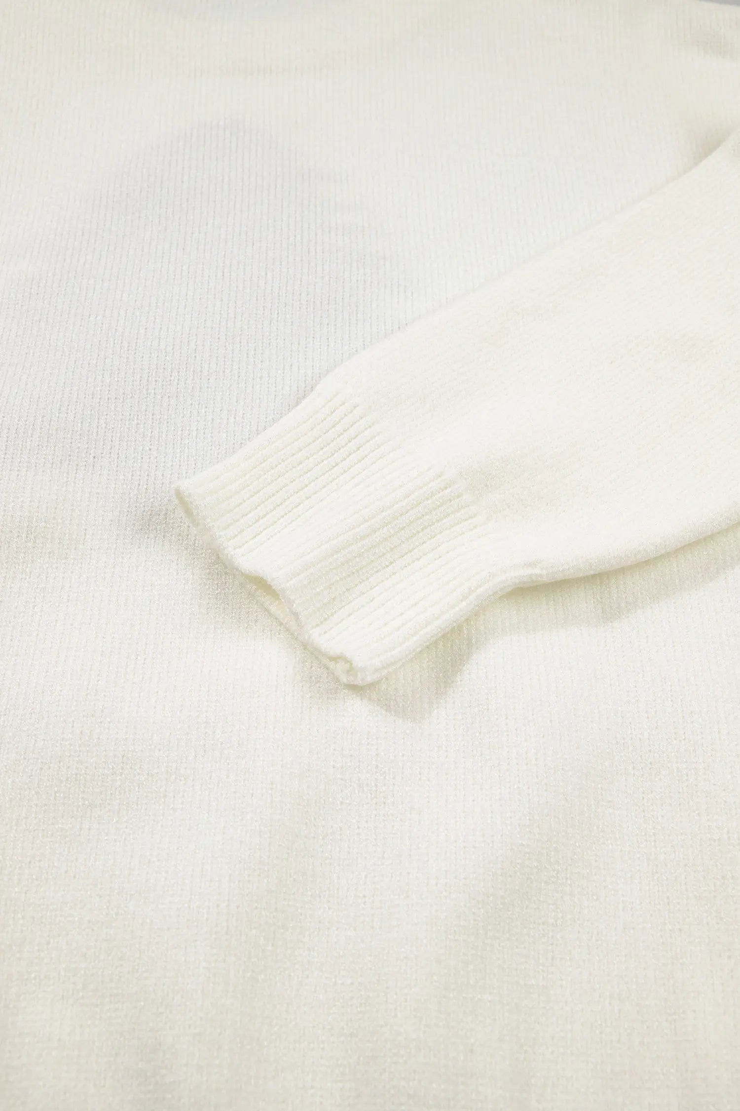 Close-up of a cream knit sweater sleeve cuff against a matching textured knit background.
