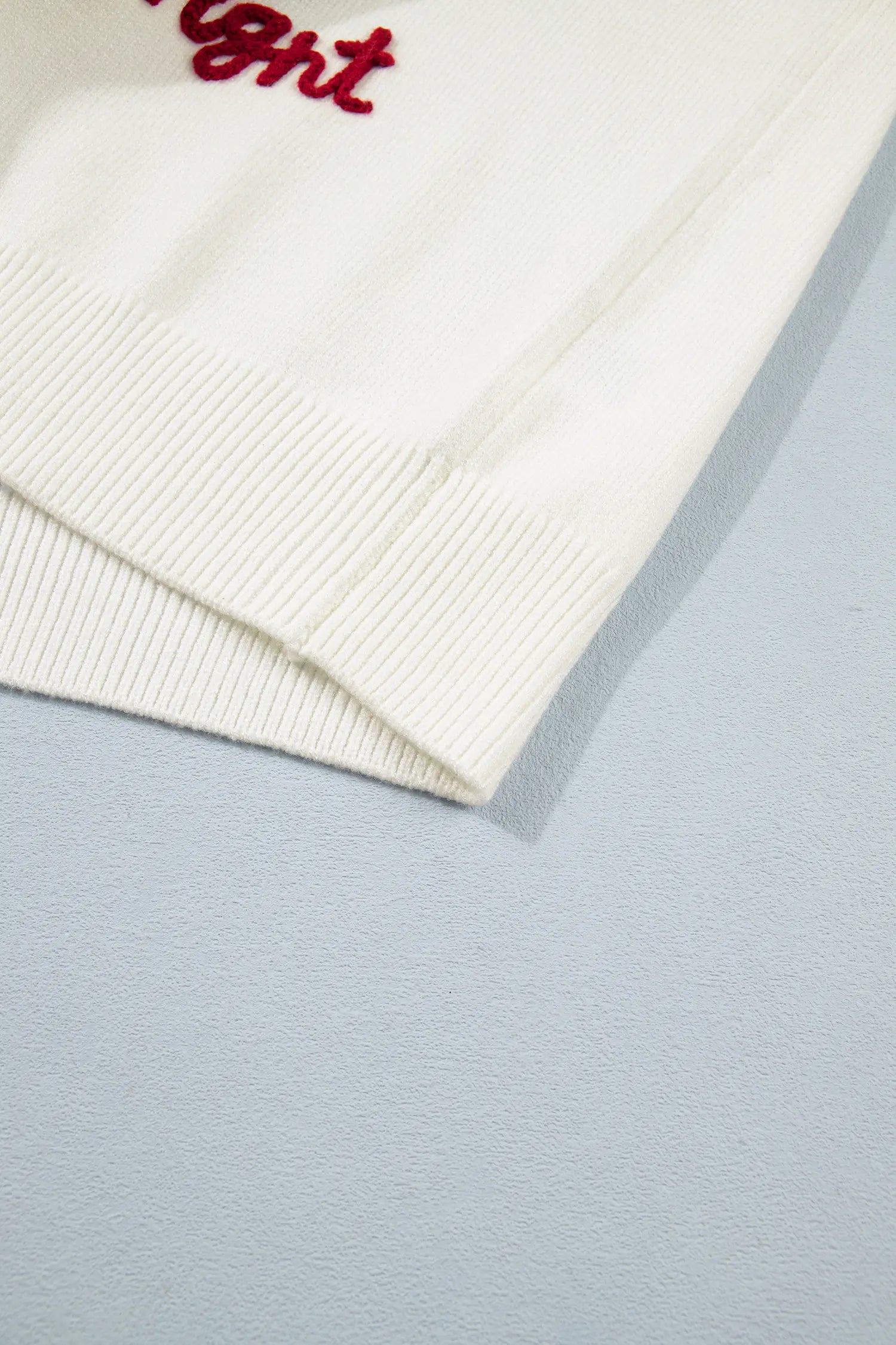 Close-up of a cream ribbed knit garment corner with red embroidered script text.