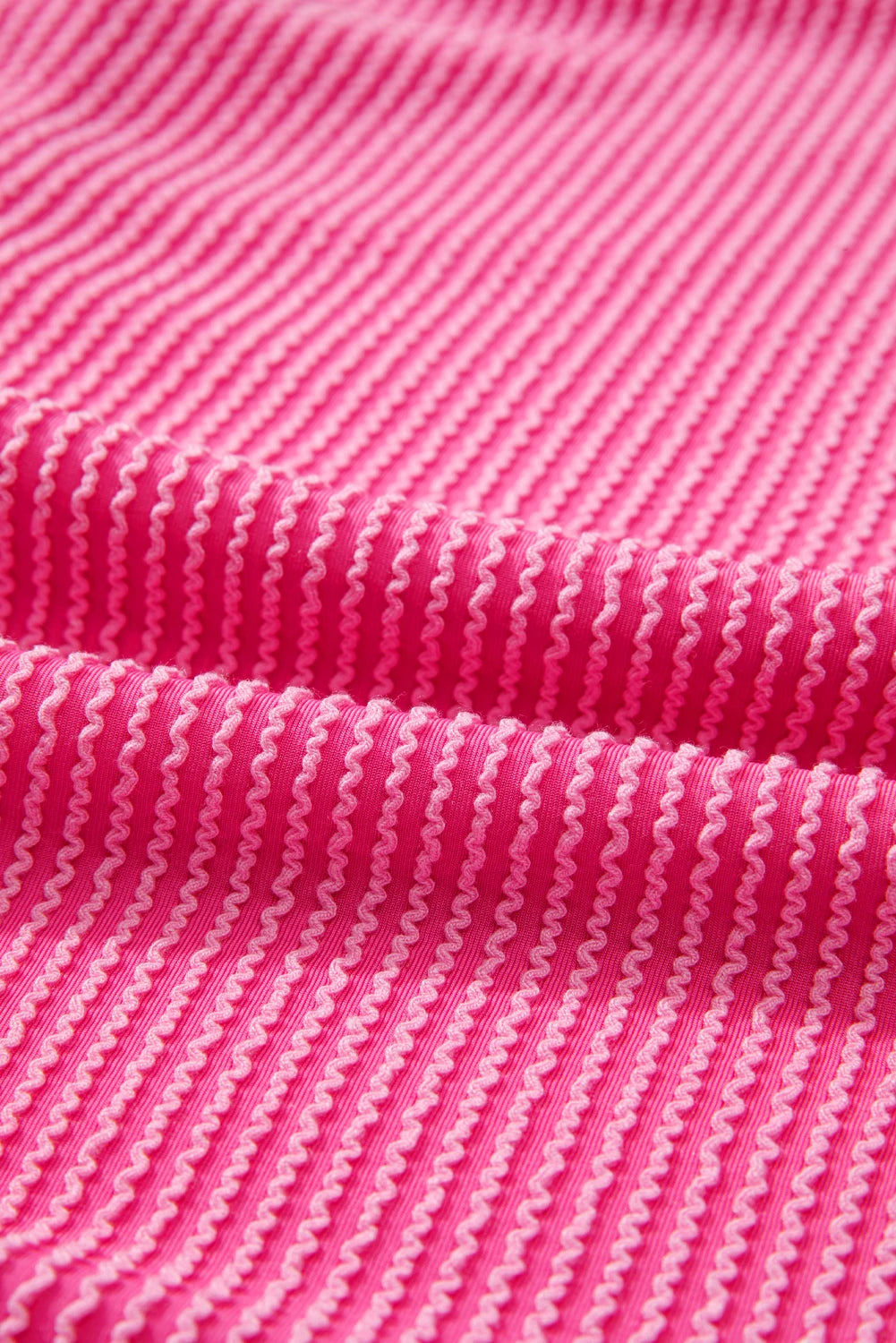 Close-up of bright pink ribbed knit fabric with wavy light pink and white vertical stripes.