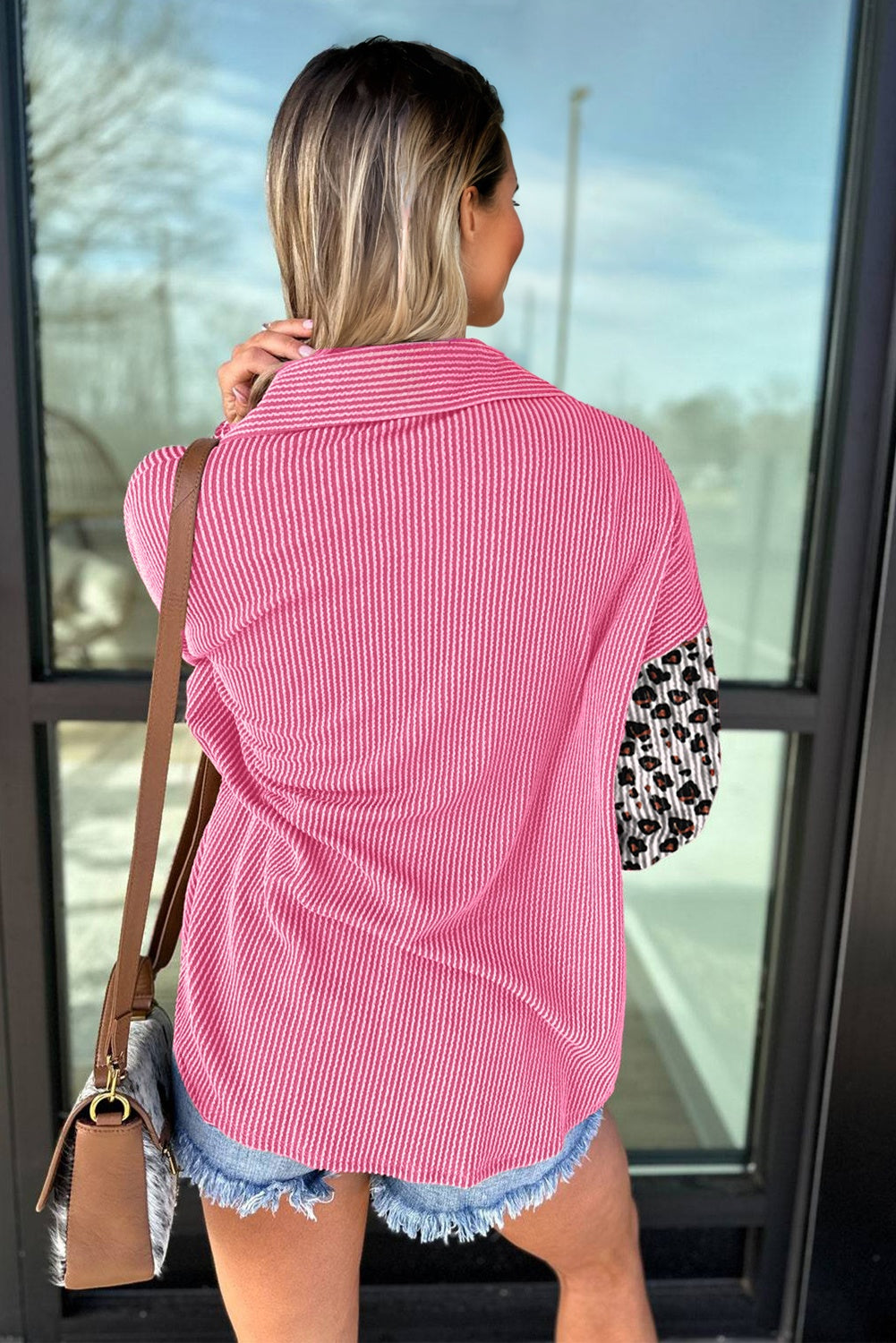 Woman in pink and white striped shirt with leopard print sleeves standing in front of glass door.