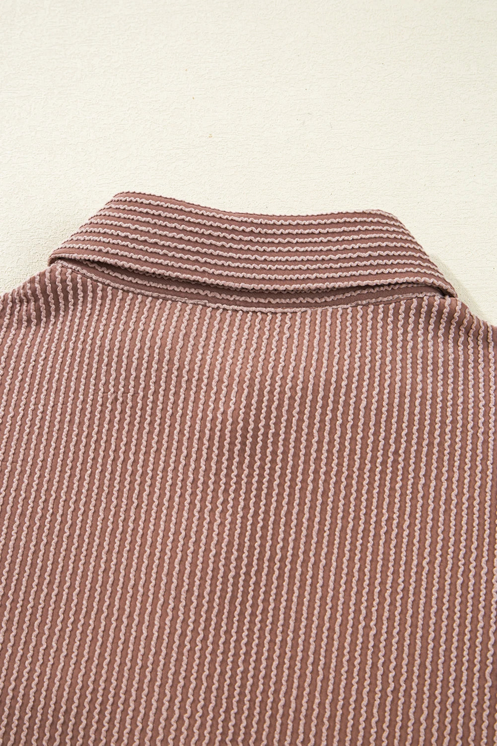 Close-up of a brown textured shirt collar on a beige background.