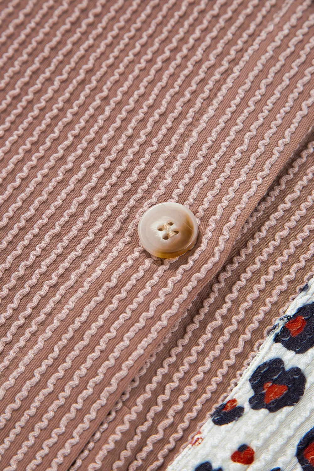 Close-up of a button on a brown striped fabric with a floral edge.