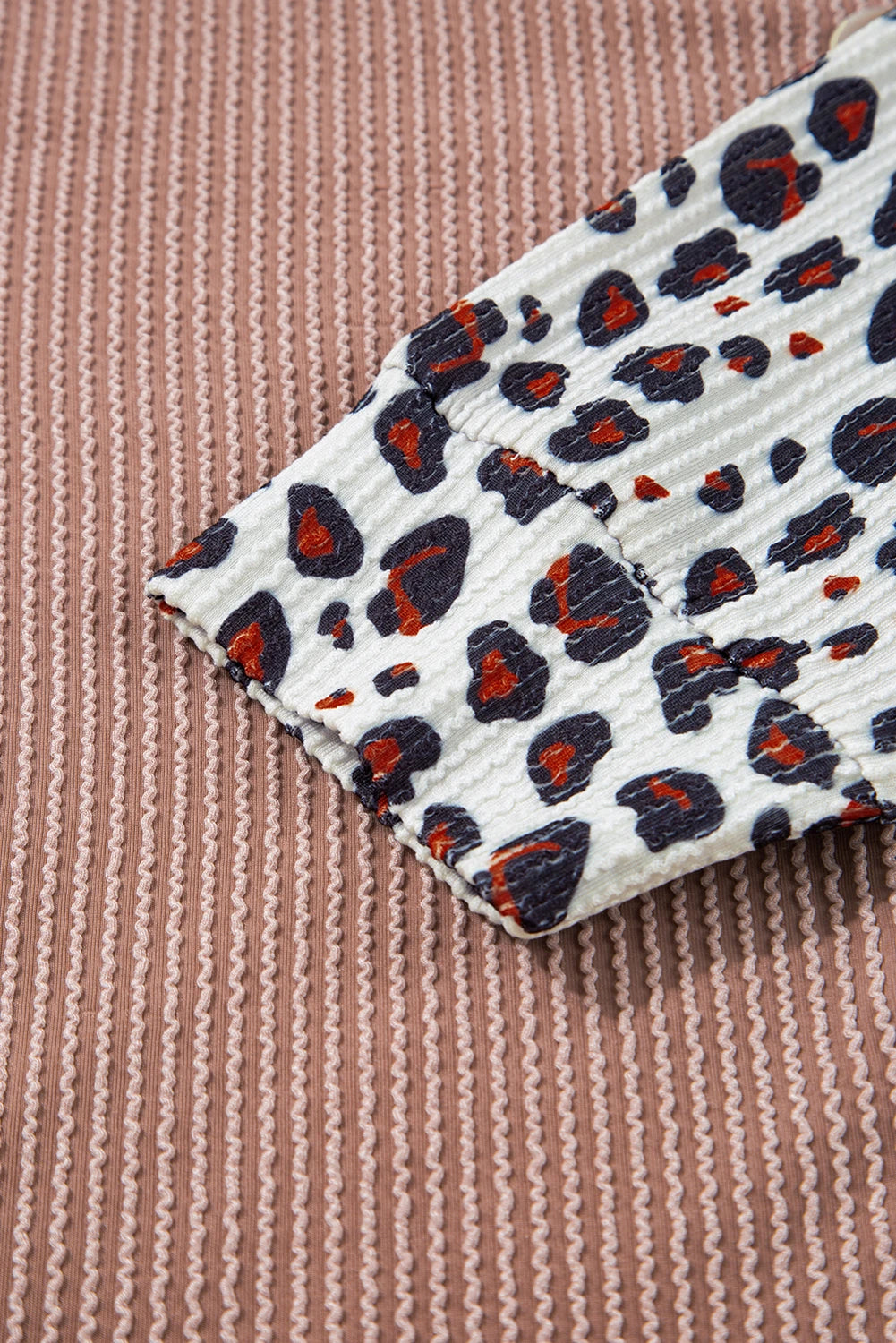 Close-up of a patterned fabric with red and black shapes on a textured brown background.
