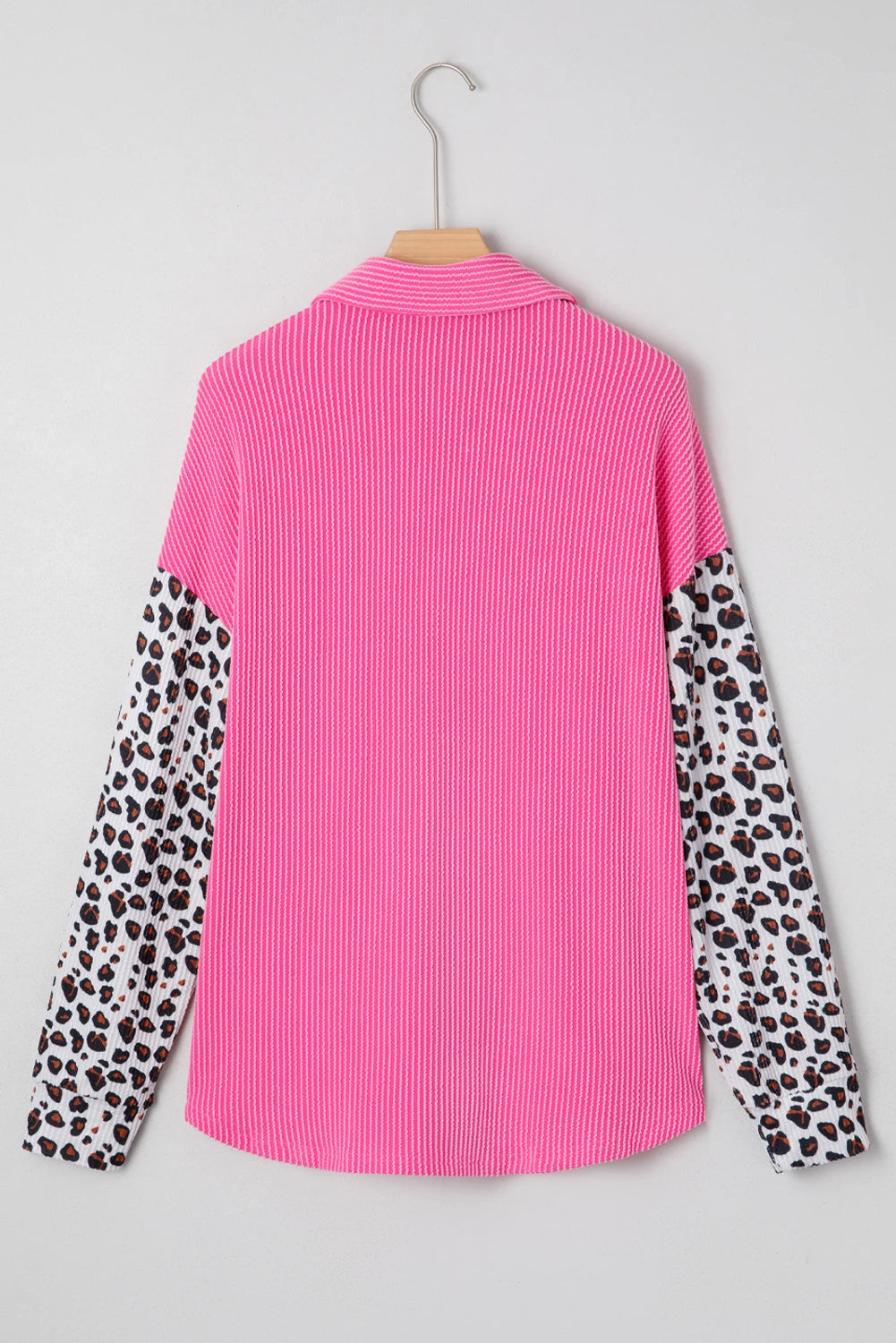 Pink long-sleeve shirt with ribbed body and leopard-print sleeves on wooden hanger against light gray.