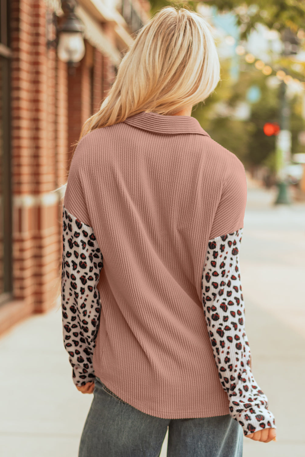 Person wearing a pink ribbed sweater over a leopard print shirt on a street.