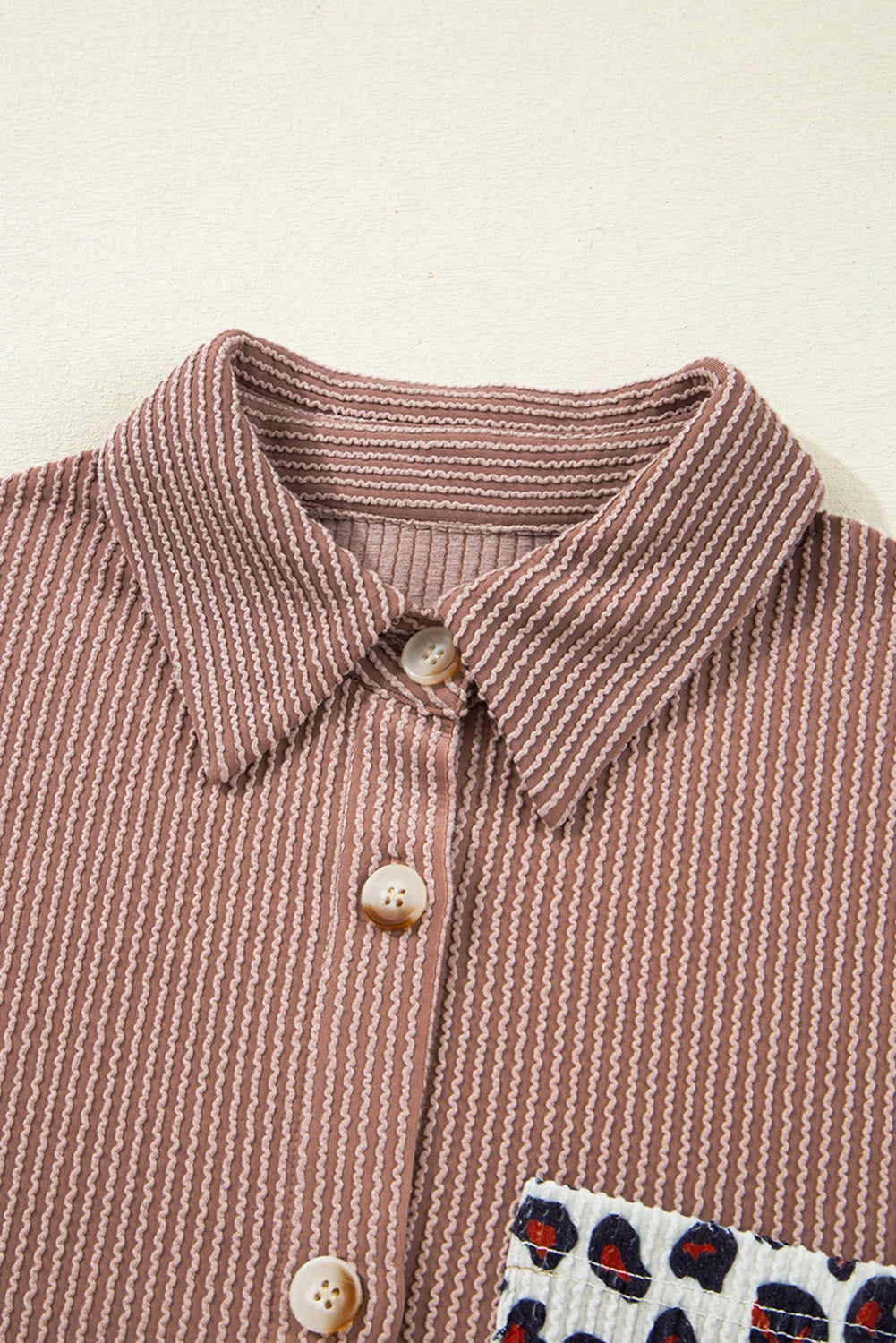 Close-up of a brown striped shirt with buttons on a beige background.