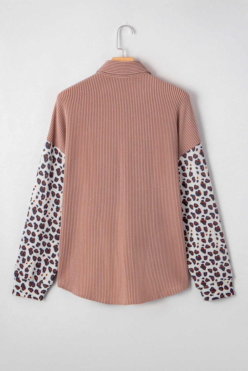 Pink ribbed shirt with leopard print sleeves on a hanger against a white background.
