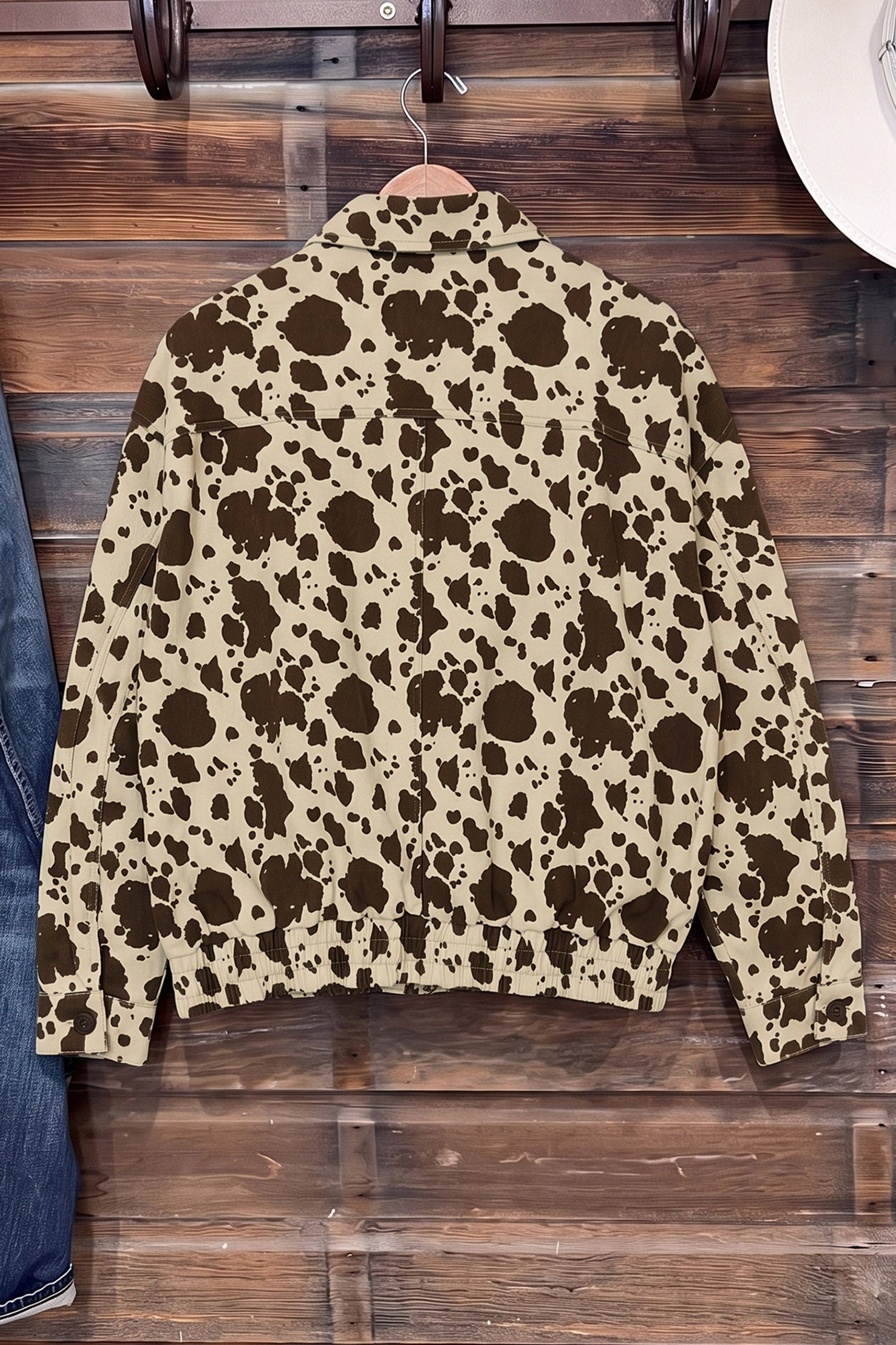 Cropped long-sleeve jacket with brown and beige cow print hanging on a wooden hanger.