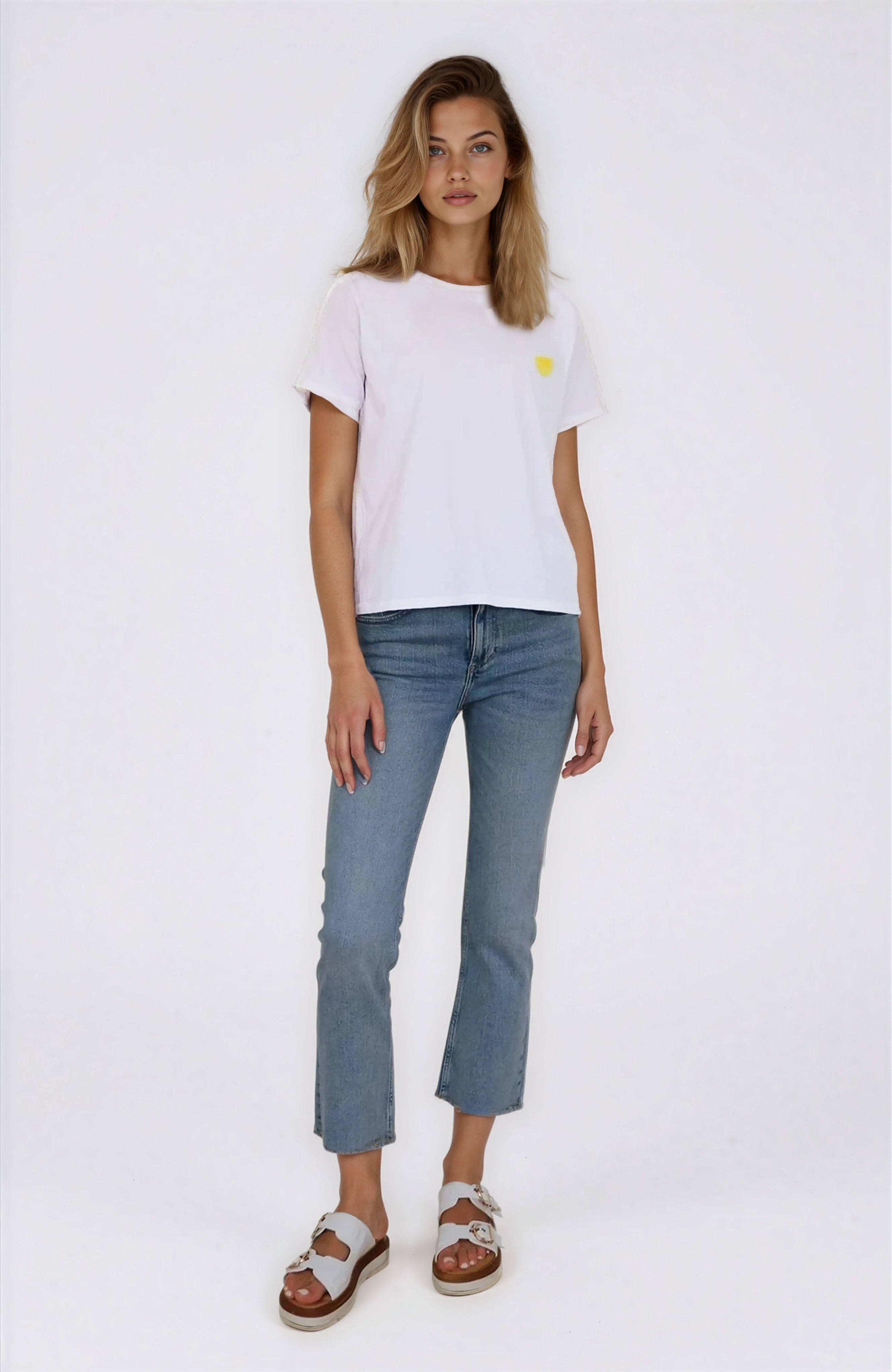 Woman wearing a white t-shirt with a small yellow logo and blue jeans on a white background