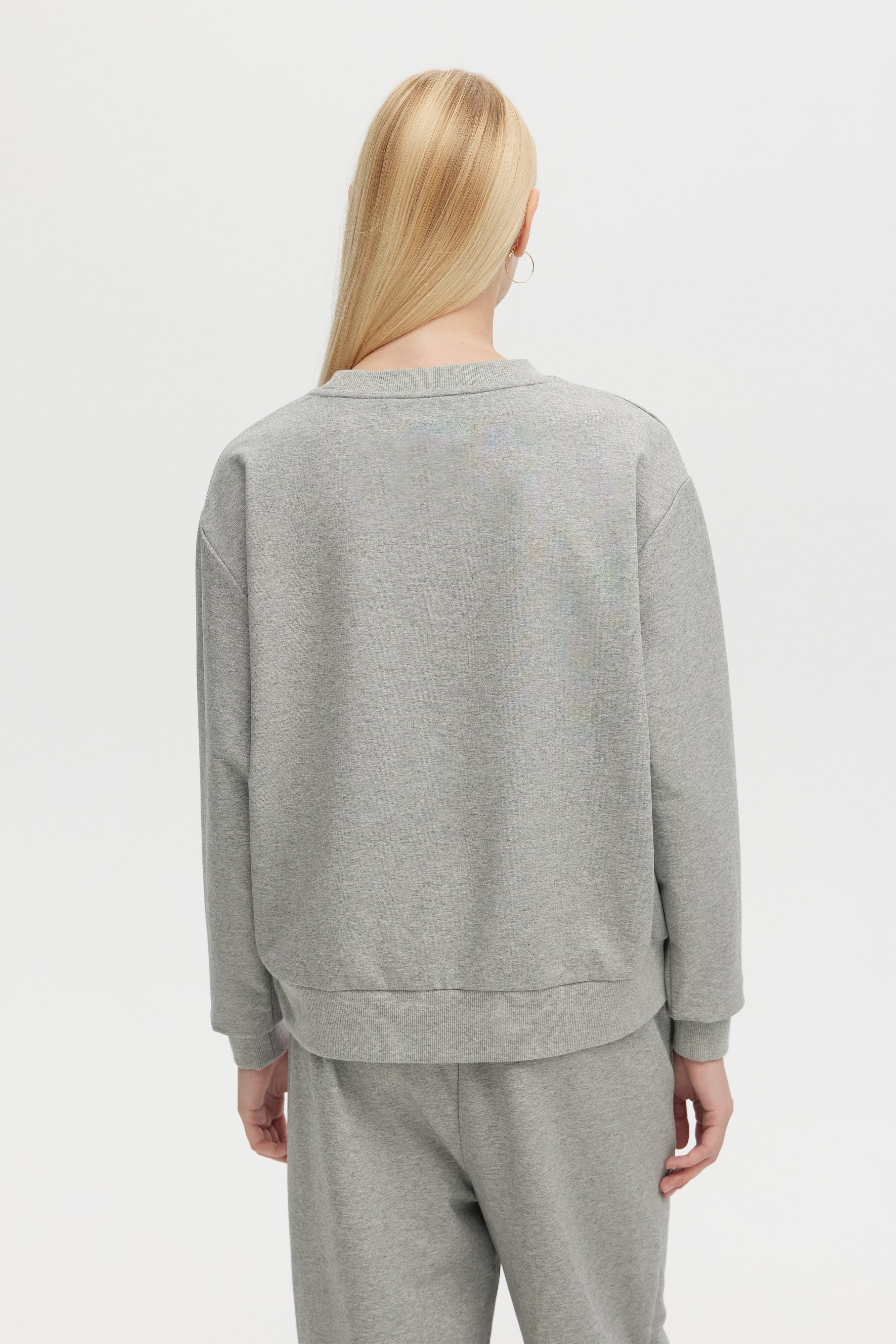 Person wearing a gray sweatshirt and pants on a white background