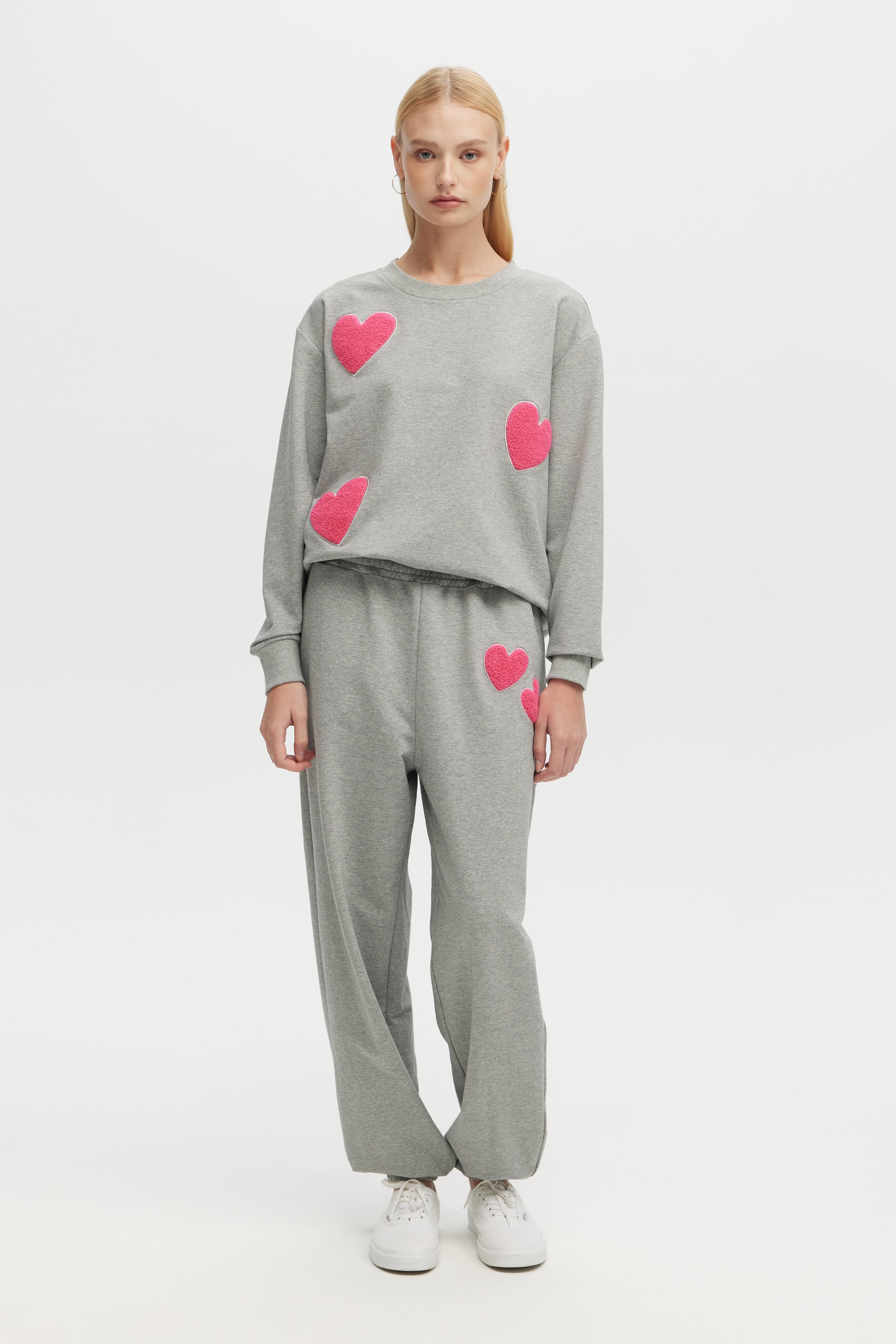 Person wearing a gray outfit with pink heart patterns on a white background