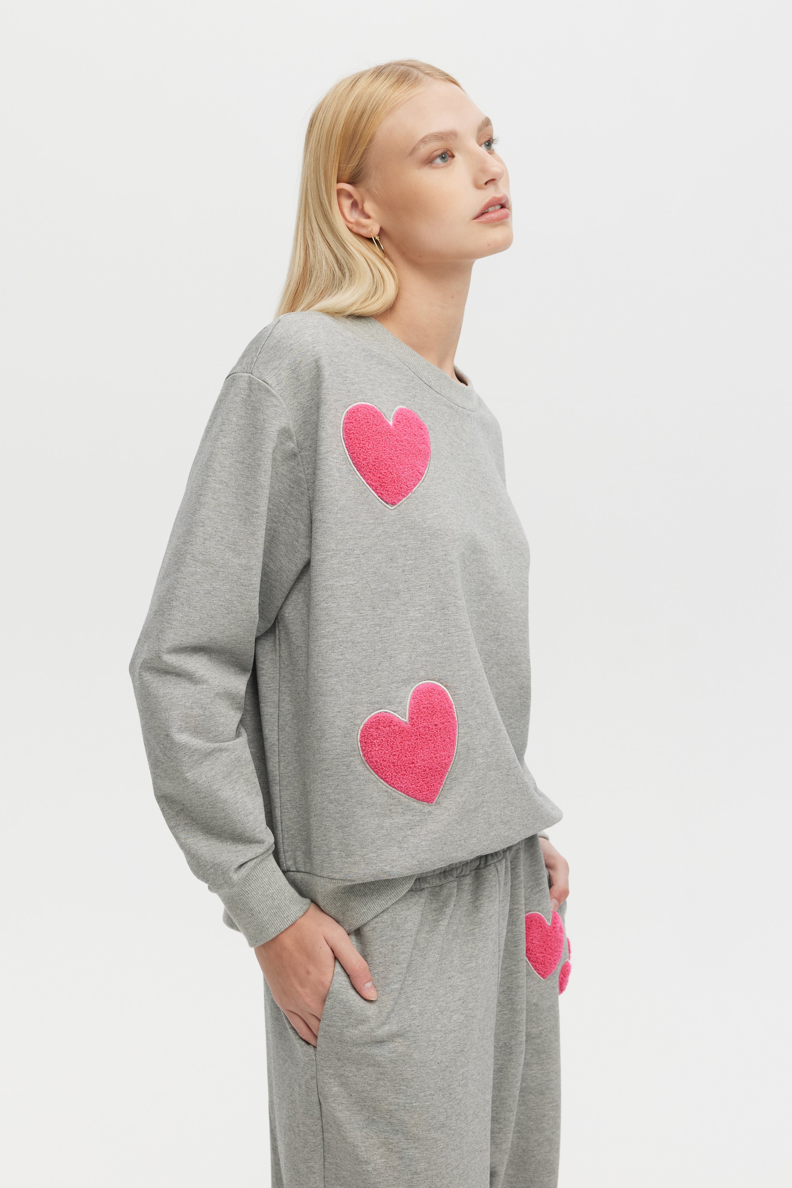 Woman wearing a gray sweatshirt with pink hearts on a white background