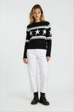 Woman wearing a black sweater with star patterns and white pants on a white background