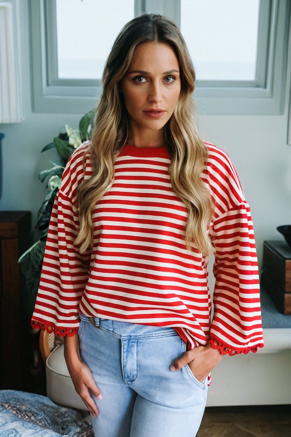 Woman wearing a red and white striped sweater and light blue jeans indoors.