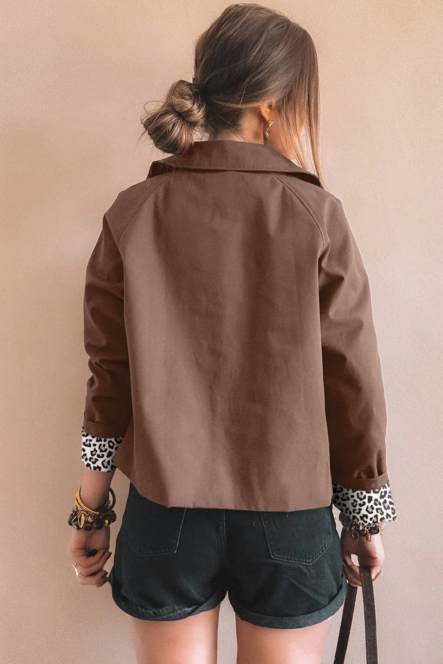Person wearing a brown jacket with leopard print cuffs against a beige background