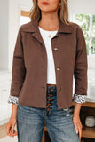 Woman wearing a brown jacket with button details, white shirt, and blue jeans indoors.