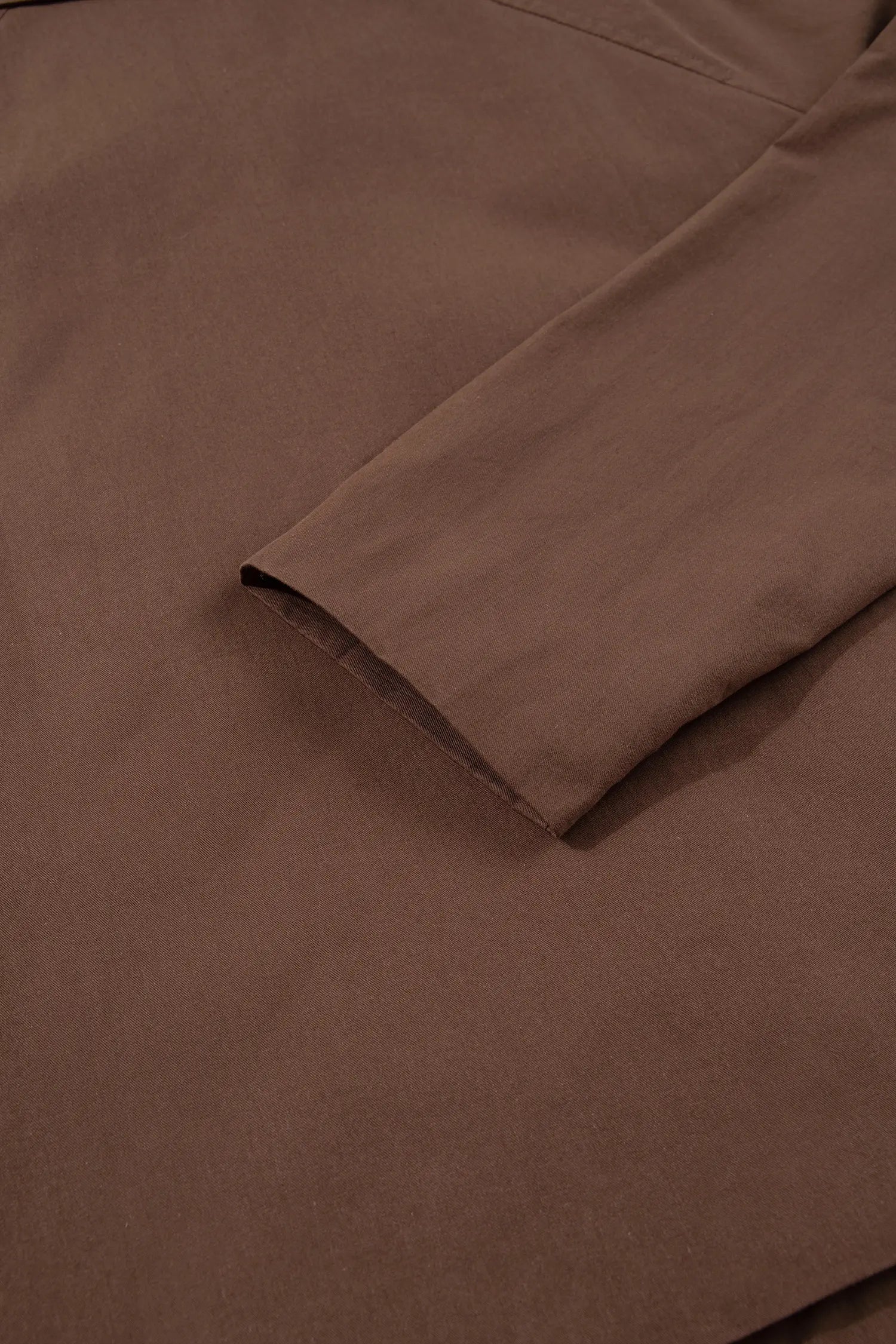 A close-up of a brown fabric garment, showing a folded sleeve or cuff with a matte finish.