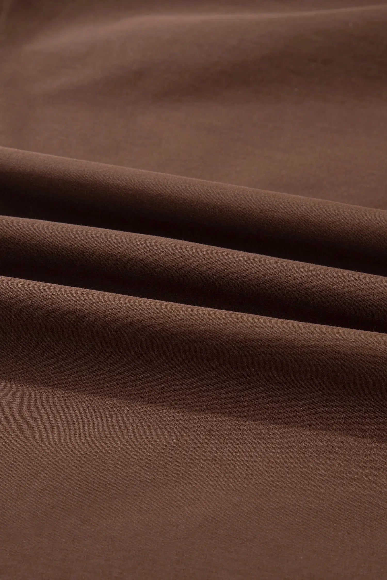 A close-up of draped brown fabric with soft folds and a smooth matte texture.