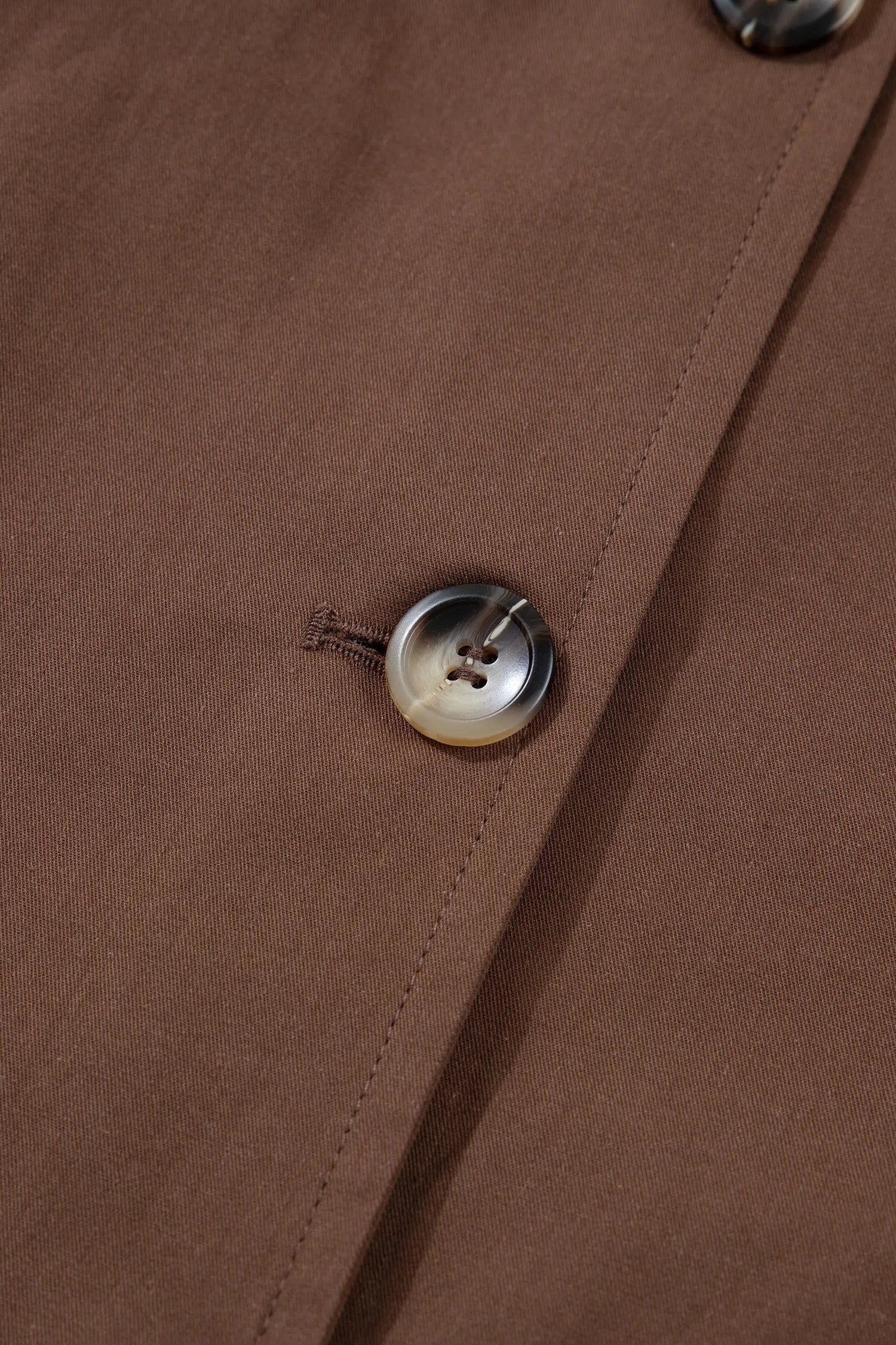 Close-up detail of a brown fabric garment with a single round button and visible stitching.