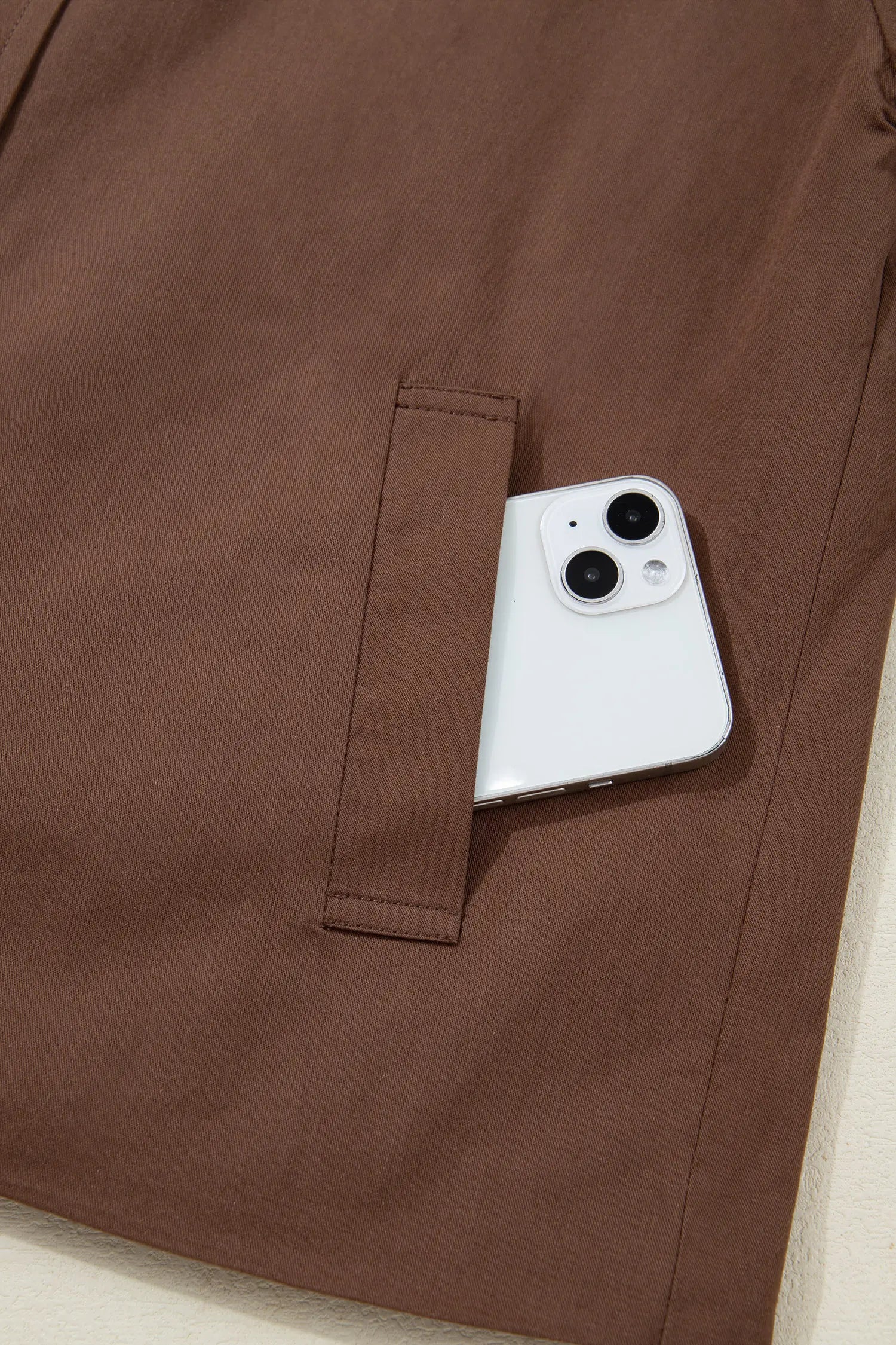 Brown jacket with a phone pocket holding a white smartphone.