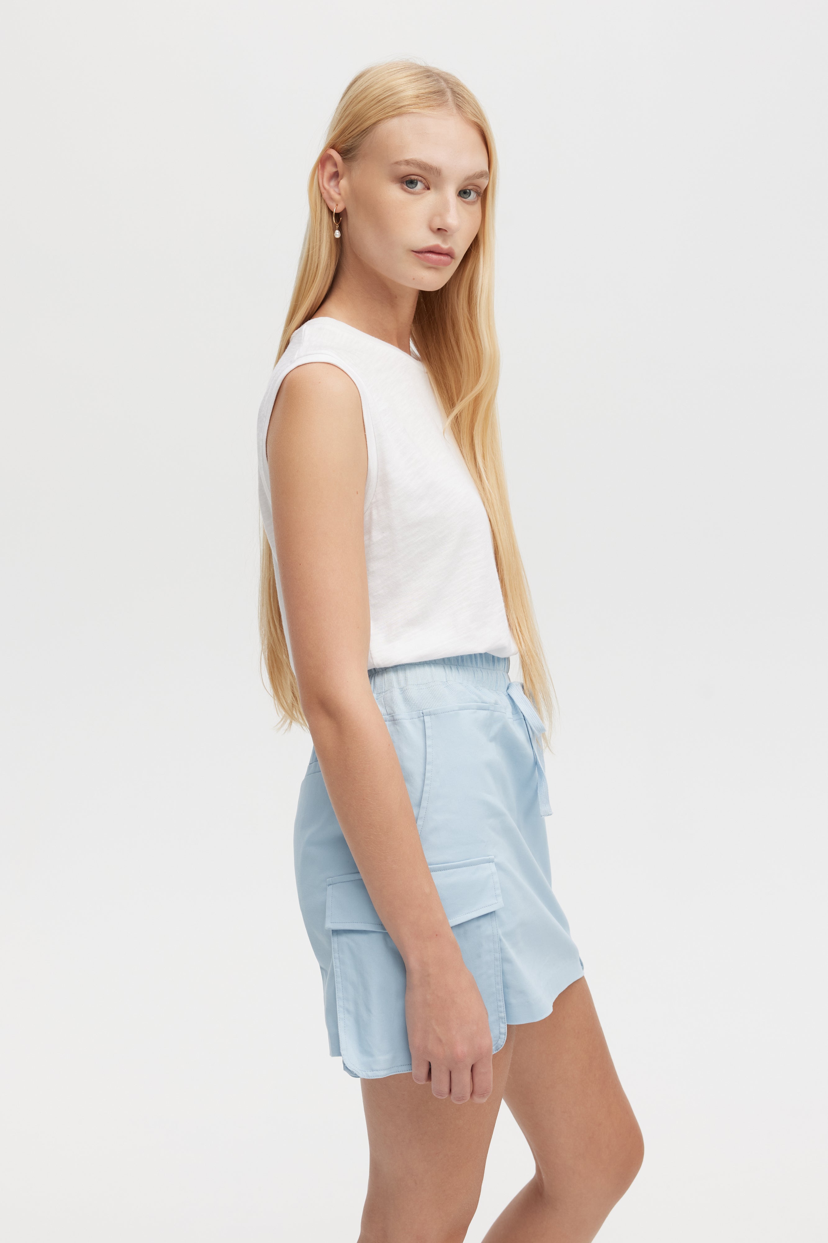 Woman wearing a white sleeveless top and light blue shorts on a white background