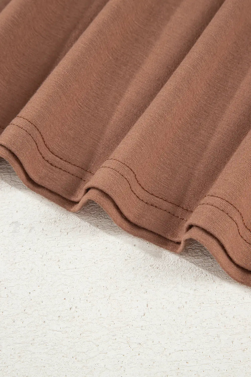 Close-up of a brown fabric with a wavy or pleated texture, laid diagonally over a white textured surface.