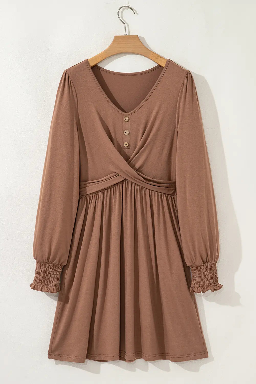 A long-sleeve brown dress with a V-neckline, three front buttons, a crossover waist, and elasticized cuffs, hanging on a wooden hanger against a plain light background.