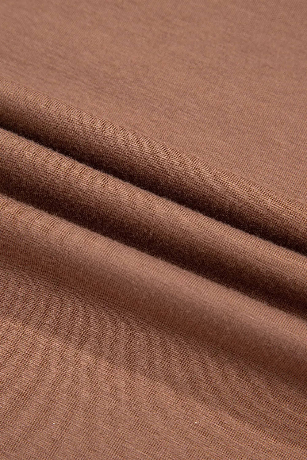 A close-up of draped brown fabric with soft folds showing its texture and color.
