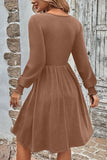 A woman wearing a long-sleeve brown dress, shown from the back in an outdoor setting with a rustic stone wall and weathered wooden door.