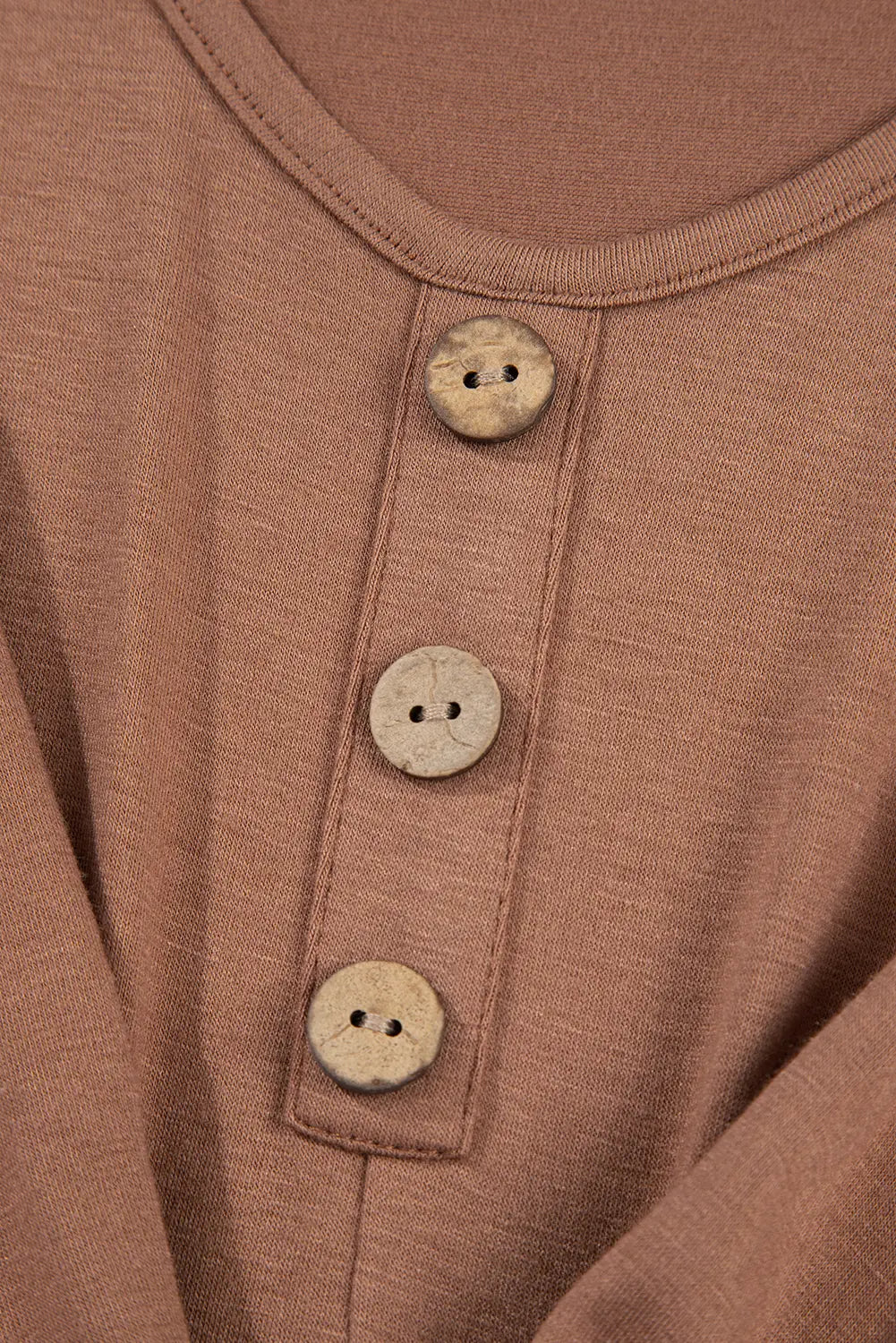 Close-up of a dusty rose or mauve-colored knit top featuring a three-button henley neckline with round, distressed off-white buttons.