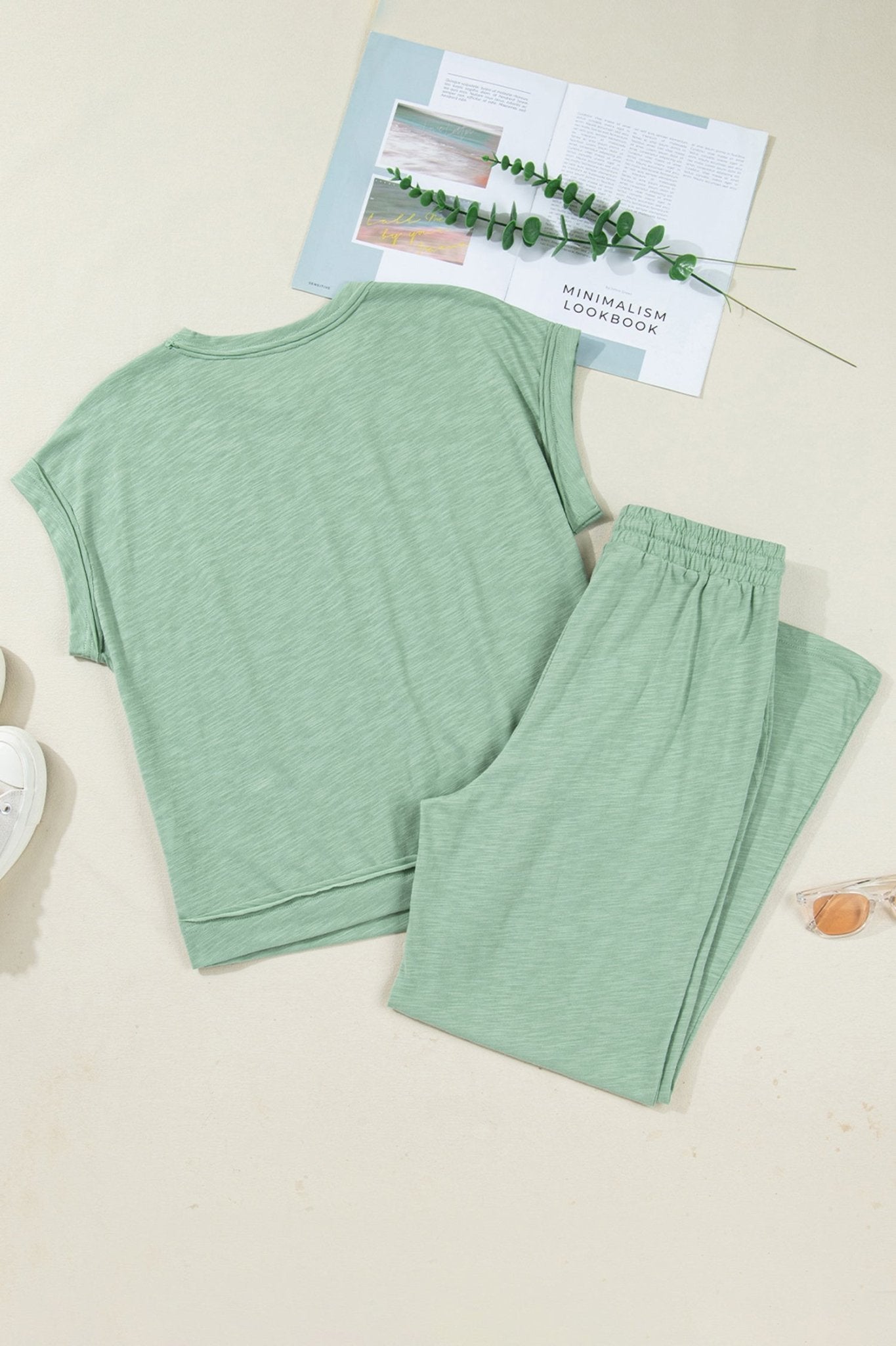 Green pajama set on a beige surface with a small plant and paper in the background.