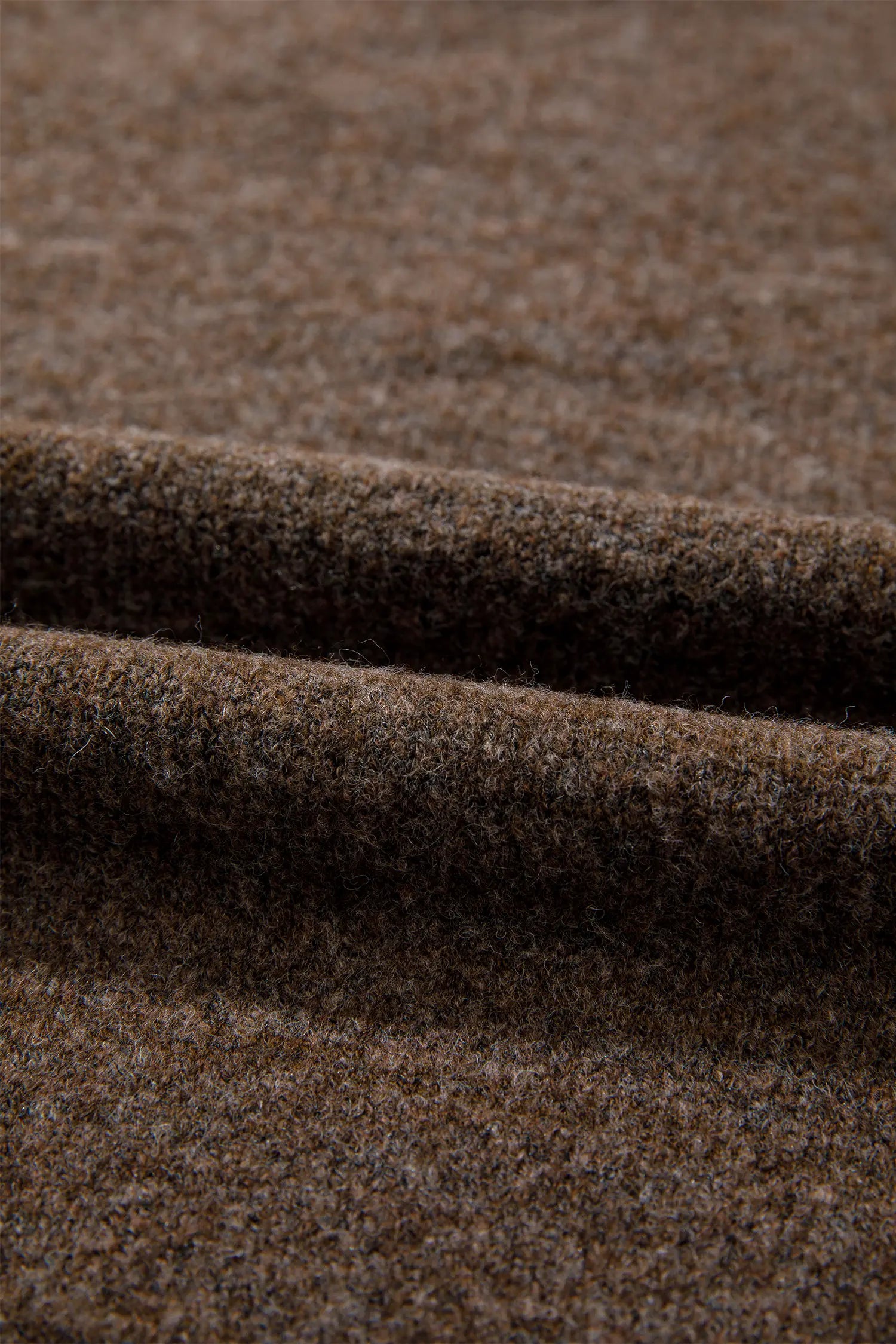 A close-up of a textured brown fabric with soft folds showing its fine woven detail.