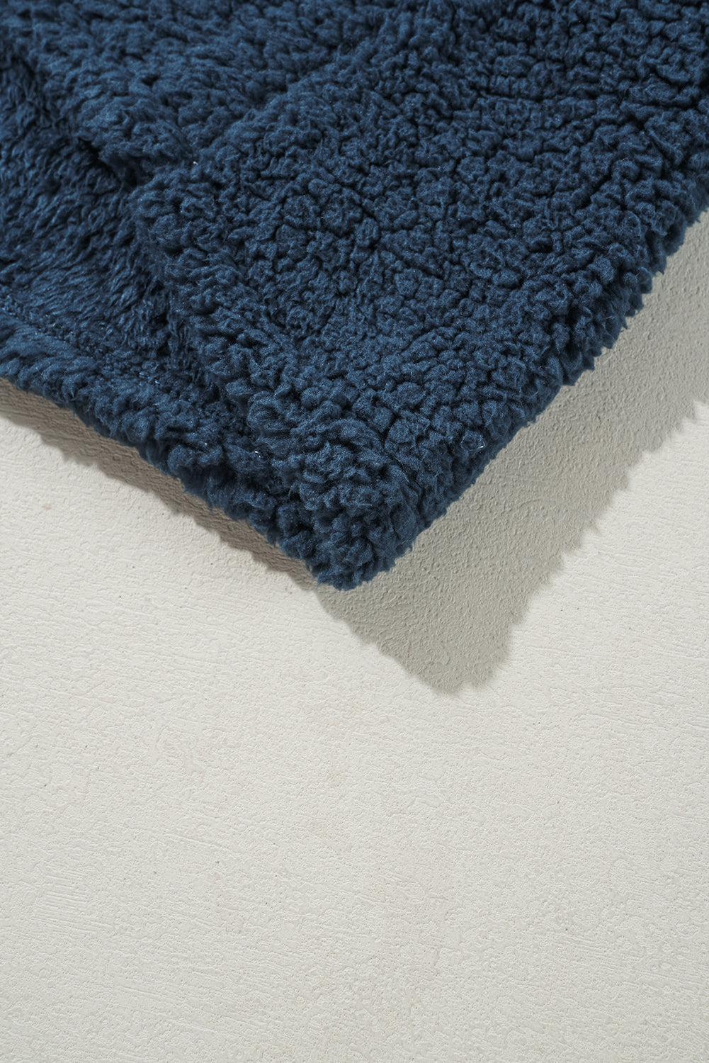 Close-up of a blue textured rug corner on a light gray floor.