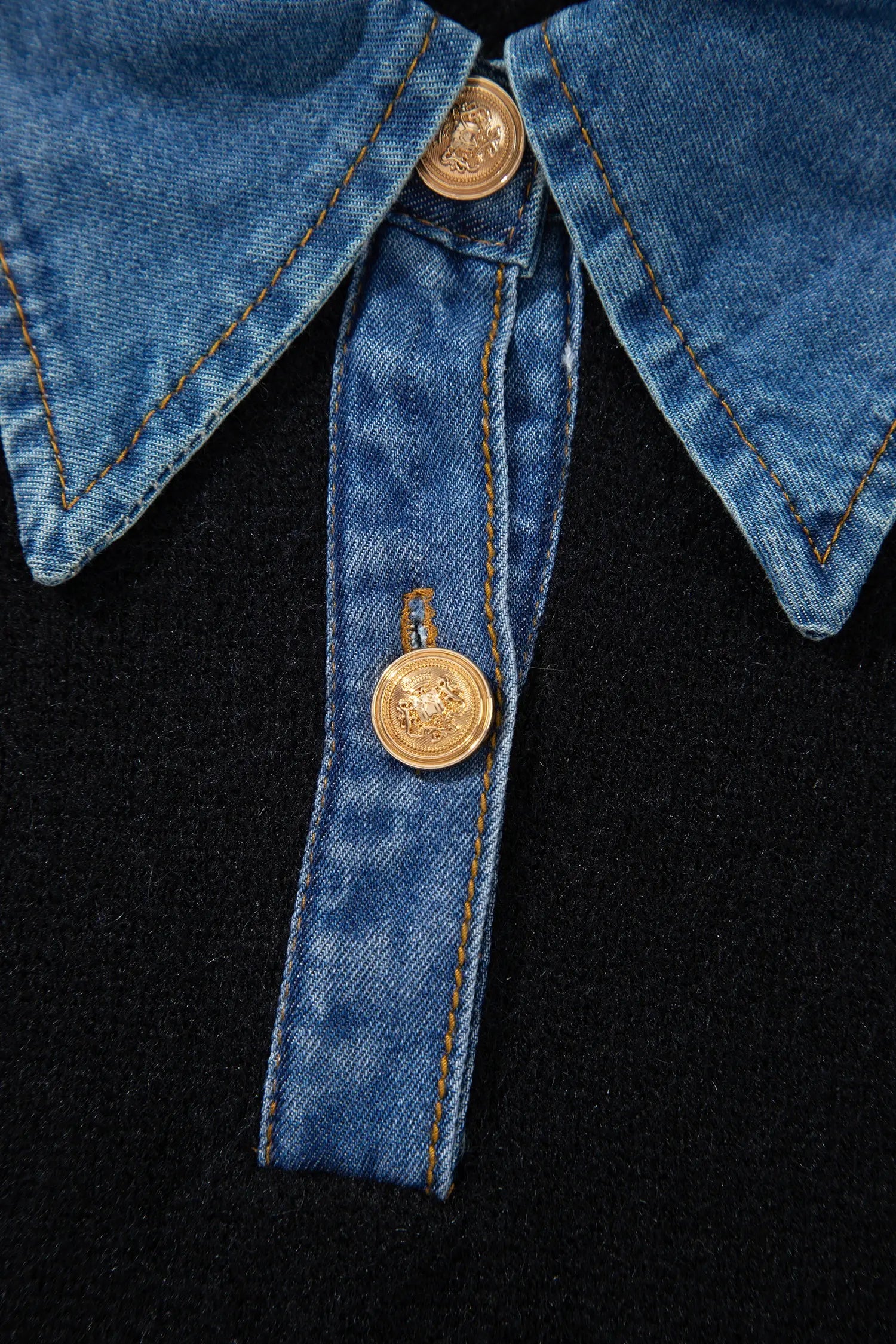 Close-up of a blue denim collar and matching tie detail on a black garment, featuring decorative gold-tone buttons.